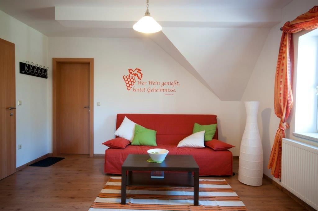 Gemütliches Gästezimmer mit rotem Sofa, Kissen, Lampe und Wandzitat.