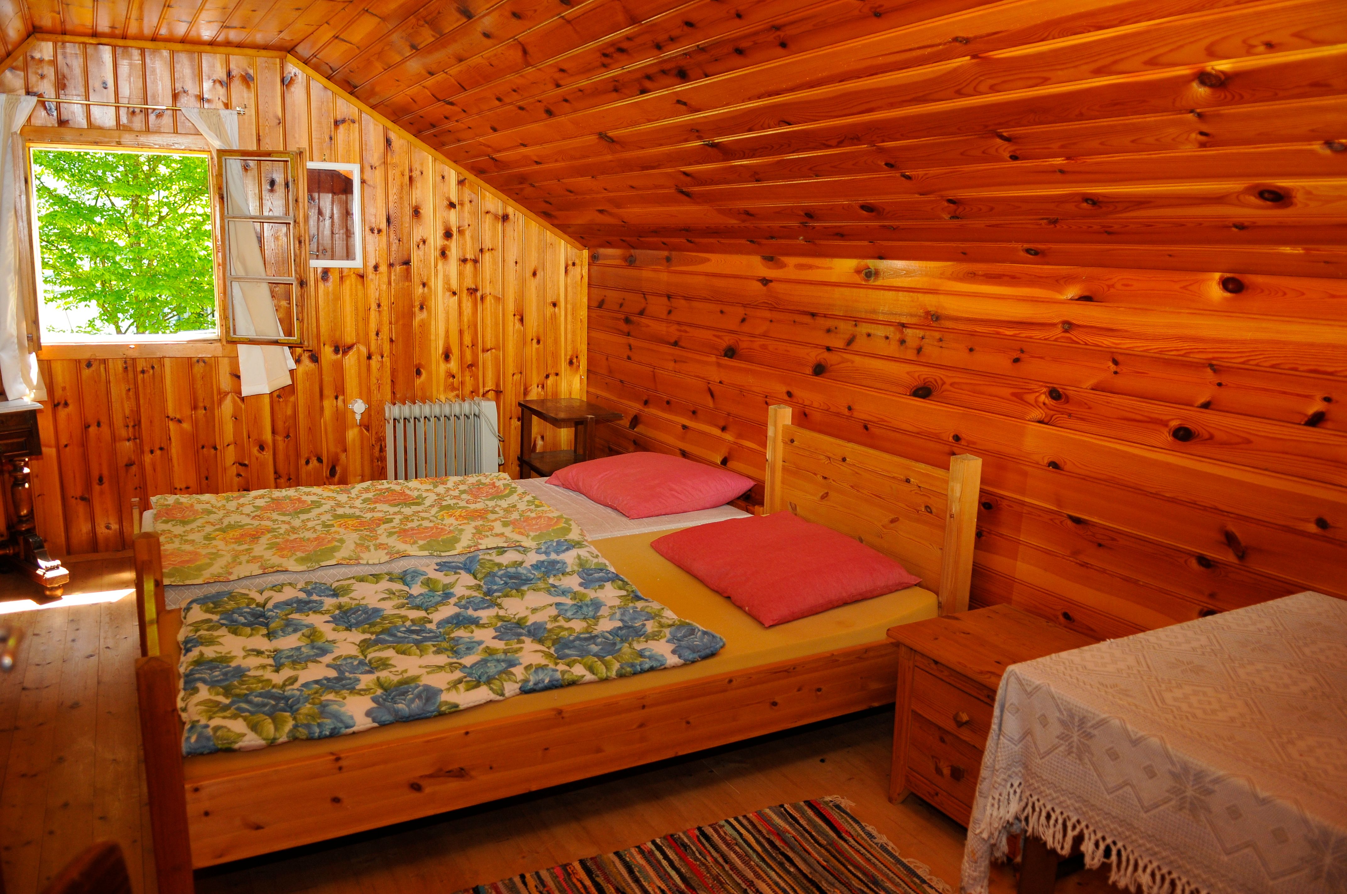 Holzvertäfeltes Schlafzimmer mit Doppelbett, bunten Decken und offenem Fenster.