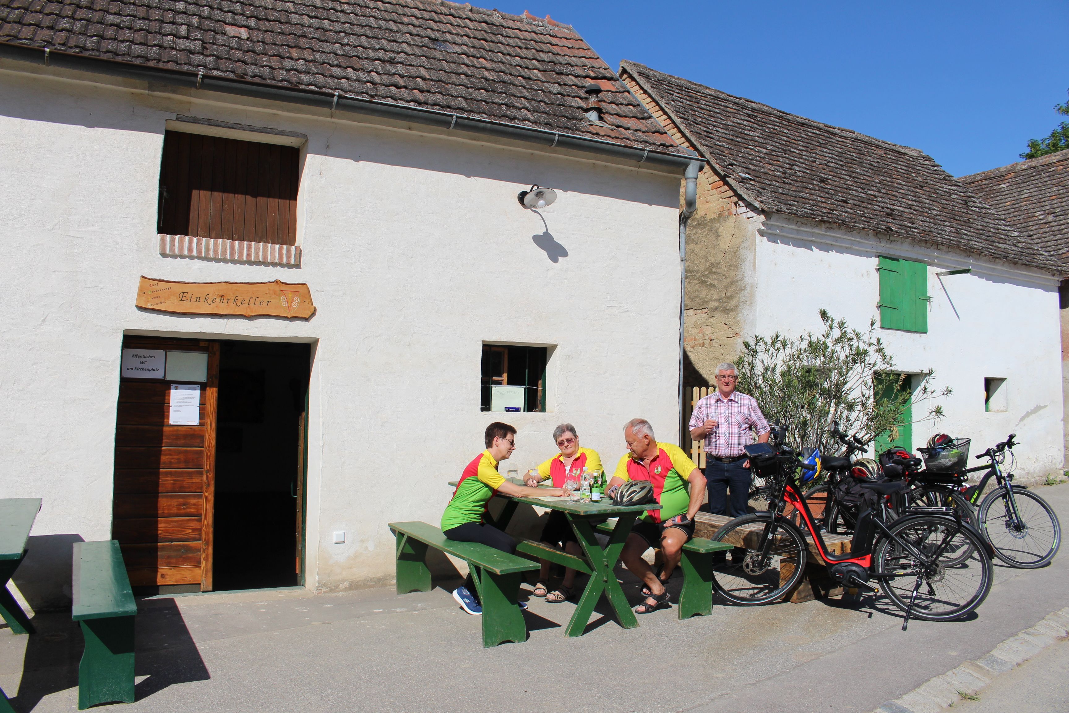 Eine Gruppe von Menschen sitzt vor dem Einkehrkeller Ottenthal an einem Tisch. Fahrräder sind daneben geparkt. Es ist ein sonniger Tag.