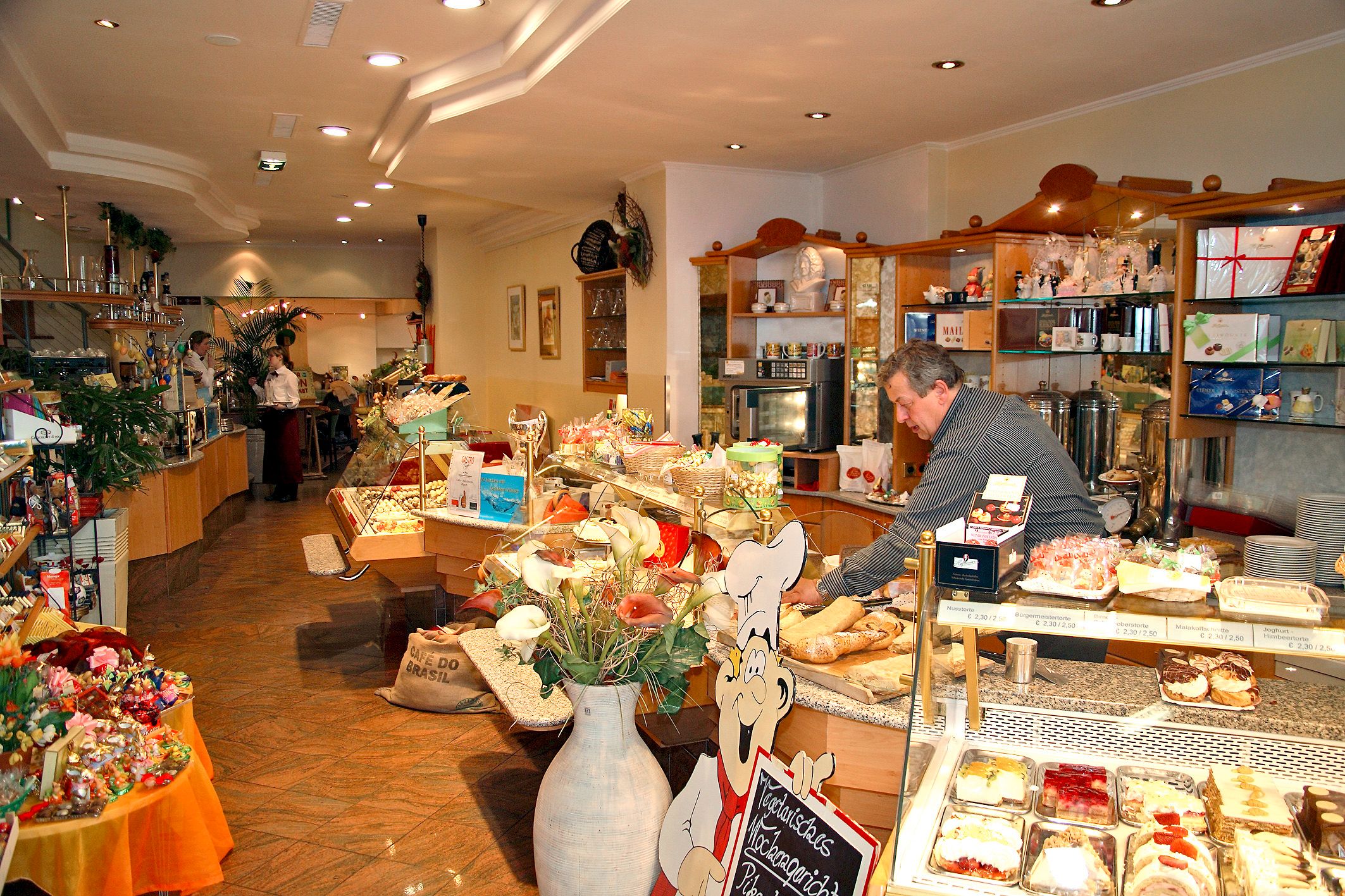 Innenansicht eines gemütlichen Cafés mit Theke voller Kuchen und Gebäck.