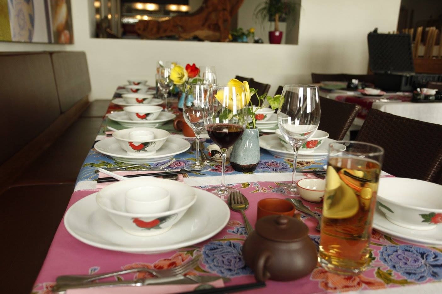 Ein gedeckter Tisch in einem Restaurant mit Geschirr, Gläsern und Blumen.