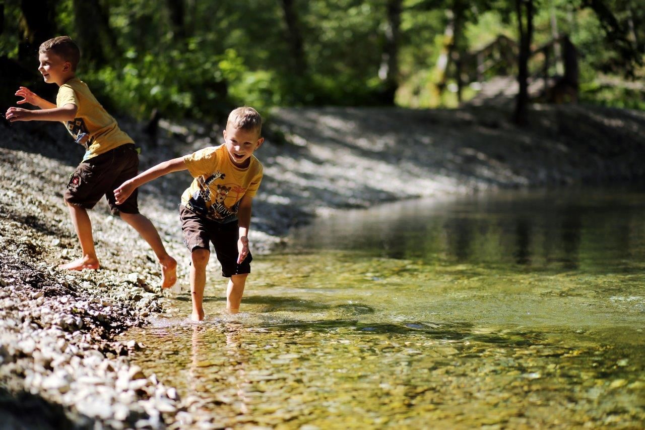 Zwei Kinder spielen am Ufer des klaren Wassers in der Natur.