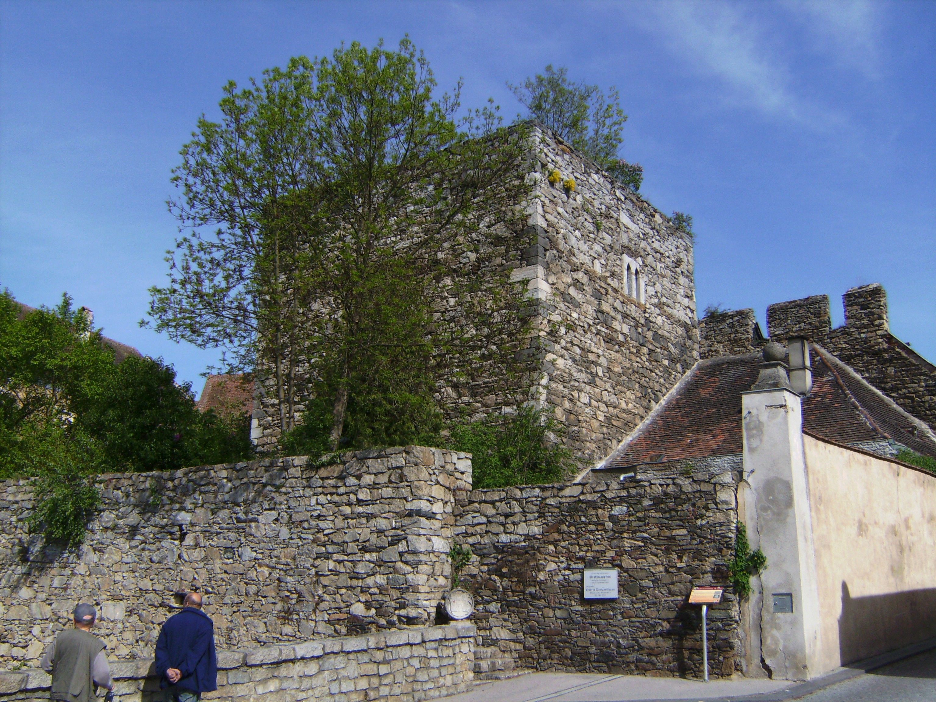 Historische Steinmauer und Turm in Drosendorf-Zissersdorf, umgeben von Bäumen und blauem Himmel.
