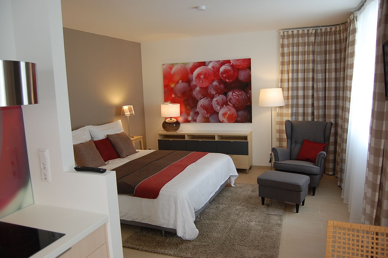 Modern eingerichtetes Schlafzimmer mit Doppelbett, Sessel und großem Bild von Weintrauben an der Wand.