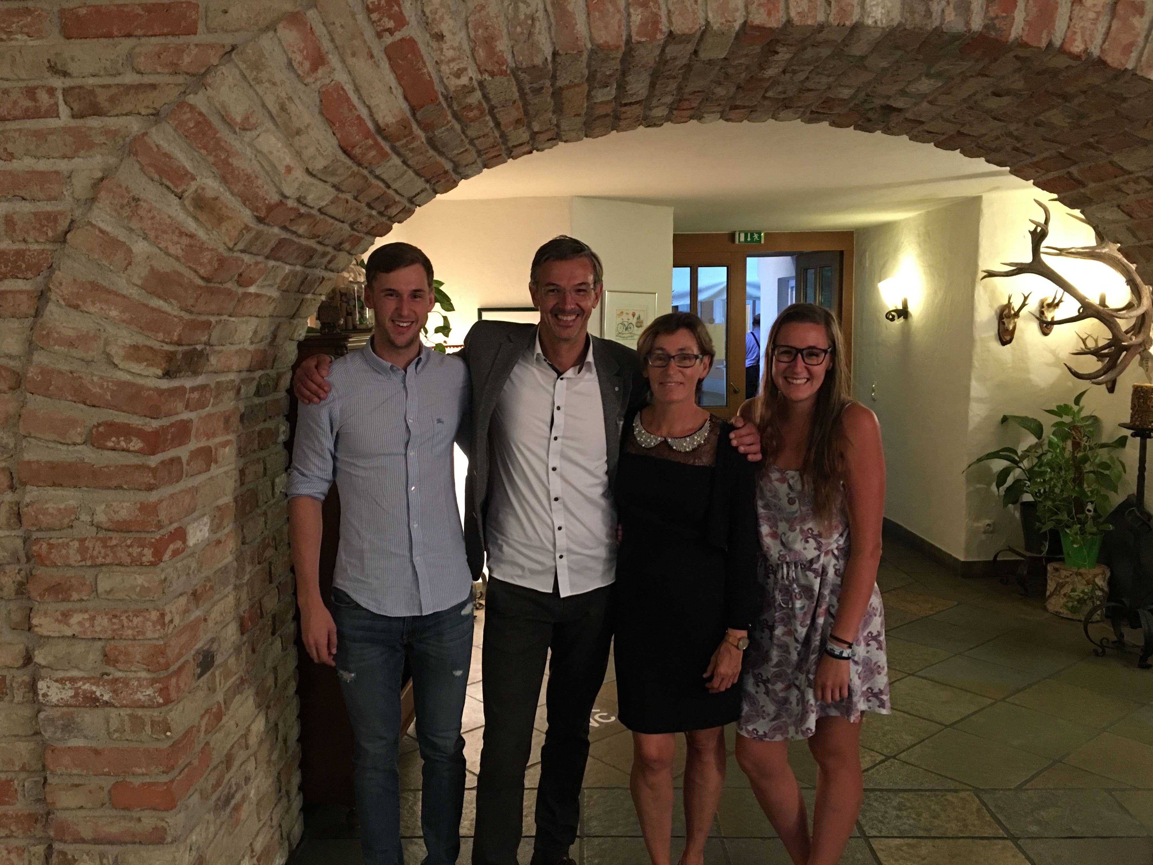 Vier Personen stehen lächelnd unter einem Backsteinbogen in einem Raum mit Jagdtrophäen an der Wand.