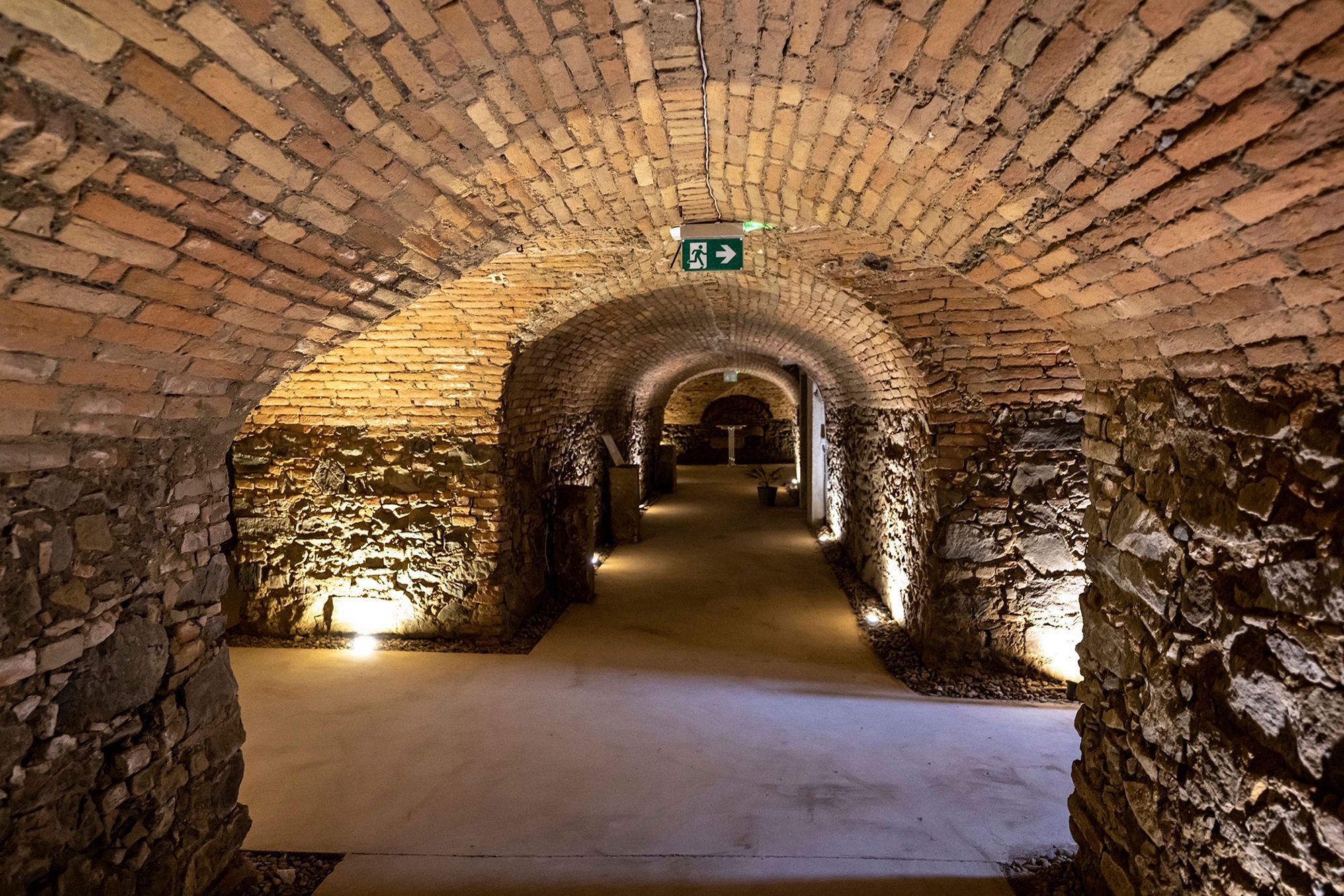 Gewölbekeller mit Backsteinmauern und Beleuchtung.