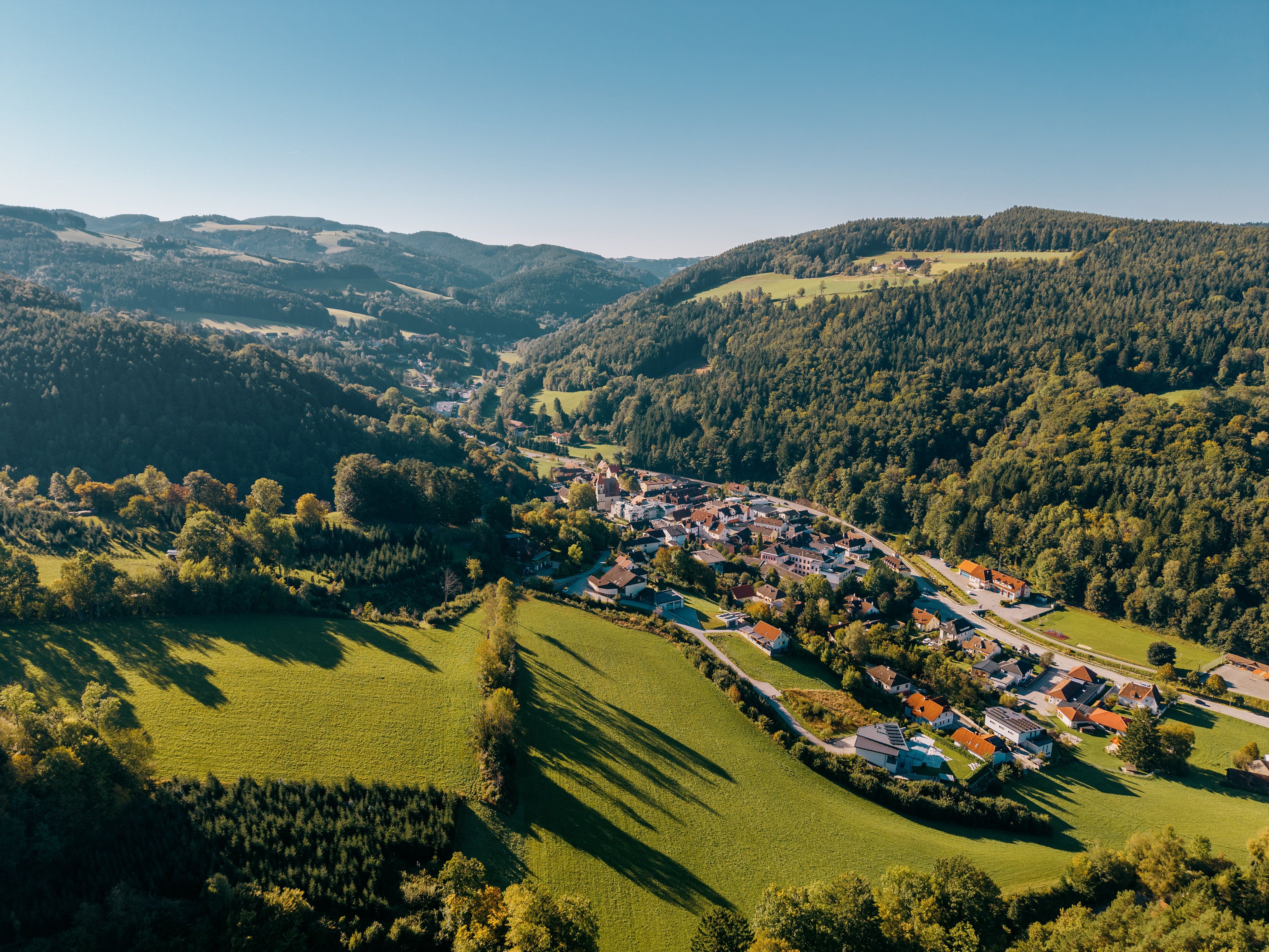 Luftaufnahme von Edlitz mit Wehrkirche, umgeben von grünen Hügeln und Wäldern.