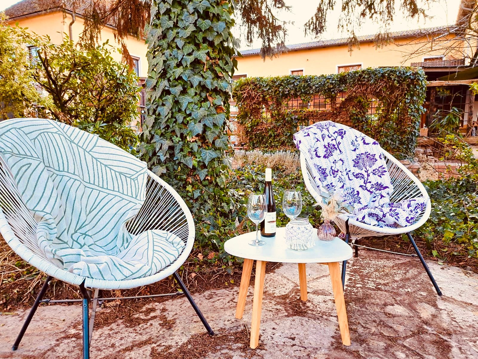 Zwei Stühle mit Decken und ein Tisch mit Weinflasche und Gläsern im Garten.