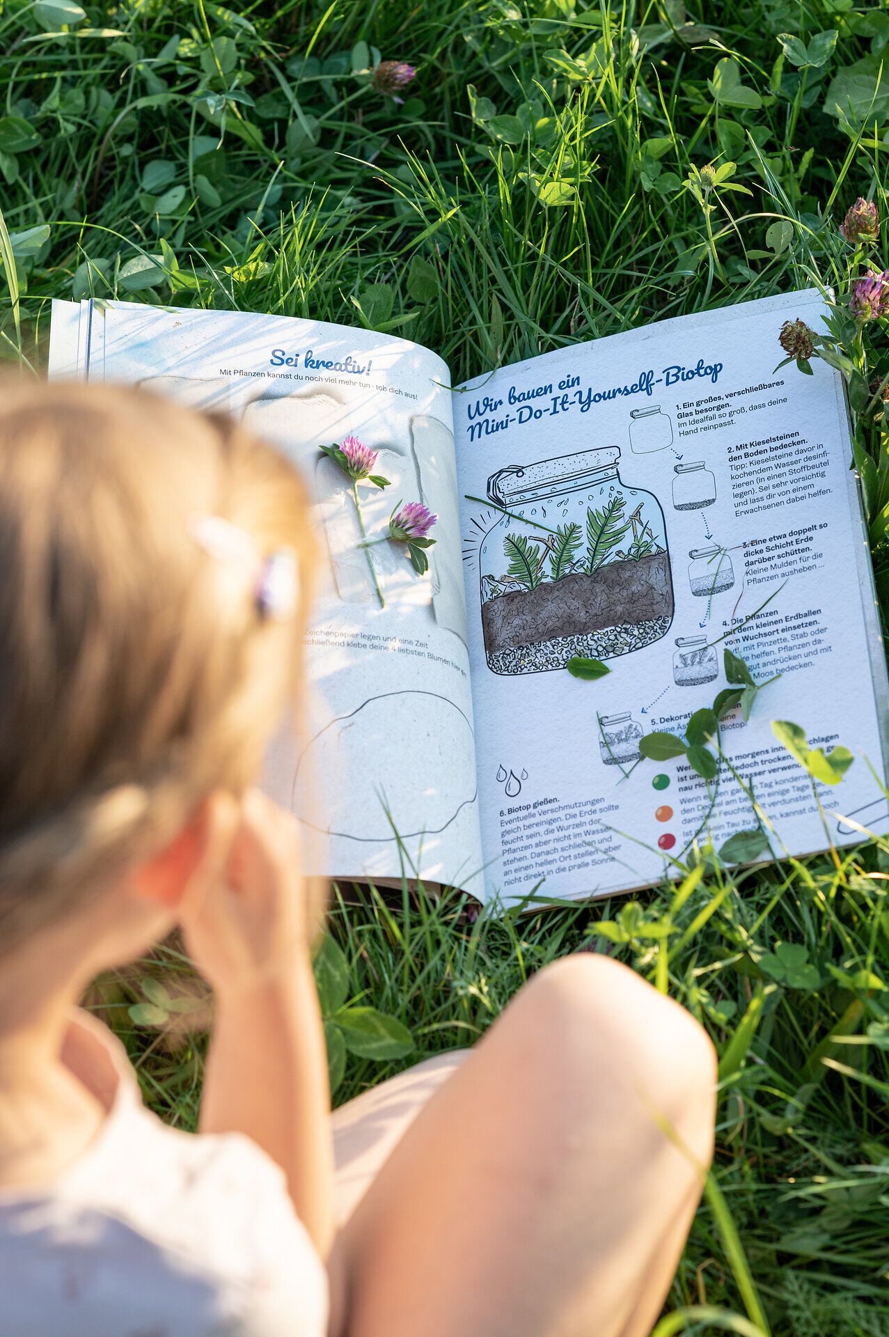 Inmitten der grünen Wiesen und bunten Blumen entdecken Kinder mit Neugier die faszinierende Welt der Pflanzen. Ein aufgeschlagenes Buch über den Bau eines Mini-Biopons inspiriert die kleinen Naturforscher, während die warmen Sonnenstrahlen eine einladende Atmosphäre schaffen. Hier wird das Lernen zum Abenteuer und die Freude an der Natur erlebbar.