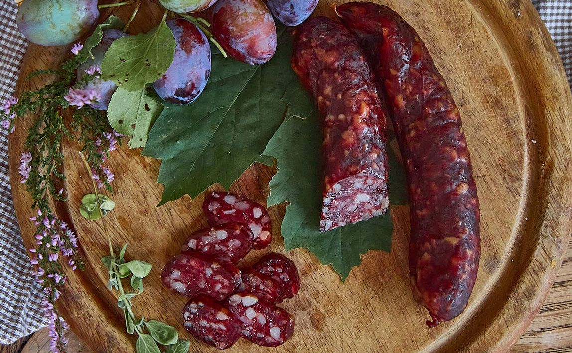 Kaminwurzn und Pflaumen auf einem Holzbrett mit grünen Blättern und Kräutern dekoriert.