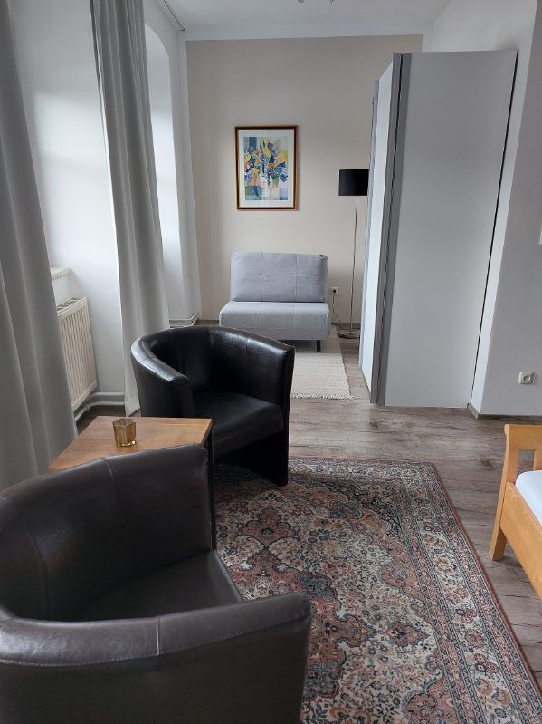 Modernes Gästezimmer mit zwei Ledersesseln, Teppich, grauem Sessel und Kunstwerk an der Wand.