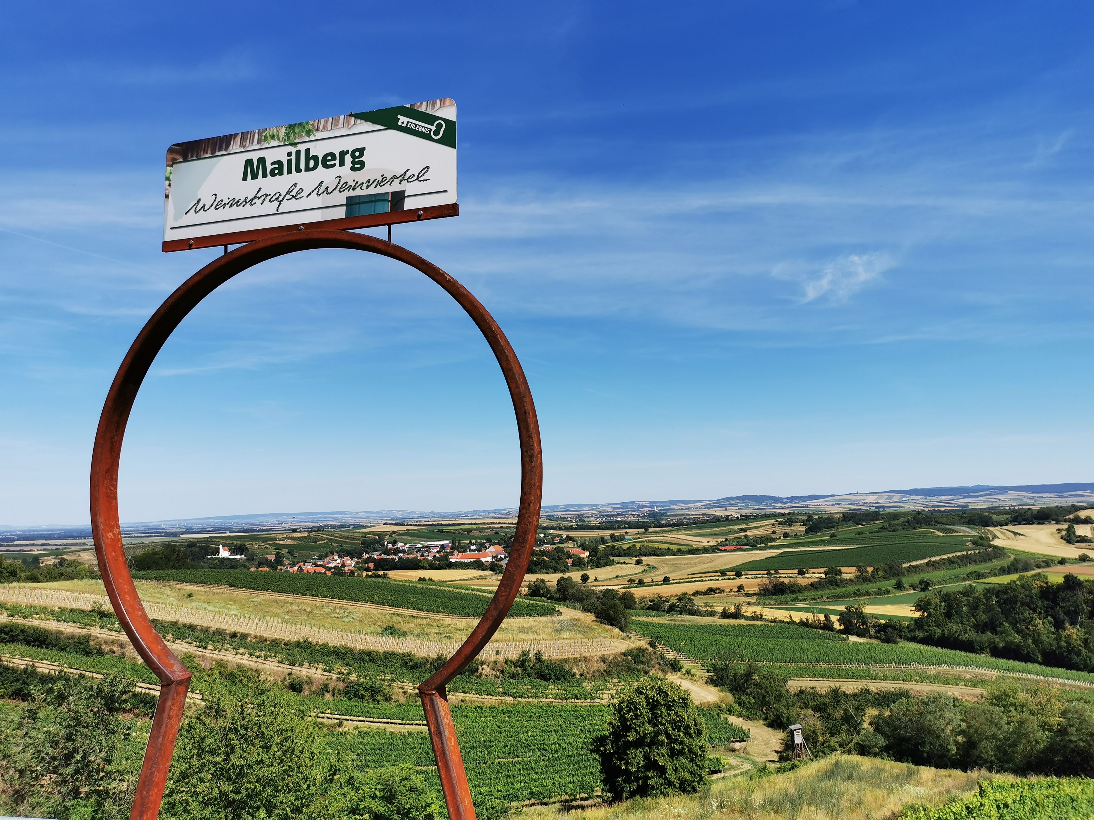 Landschaft mit Weinbergen und einem Schild mit der Aufschrift 'Mailberg Weinstraße Weinviertel'.