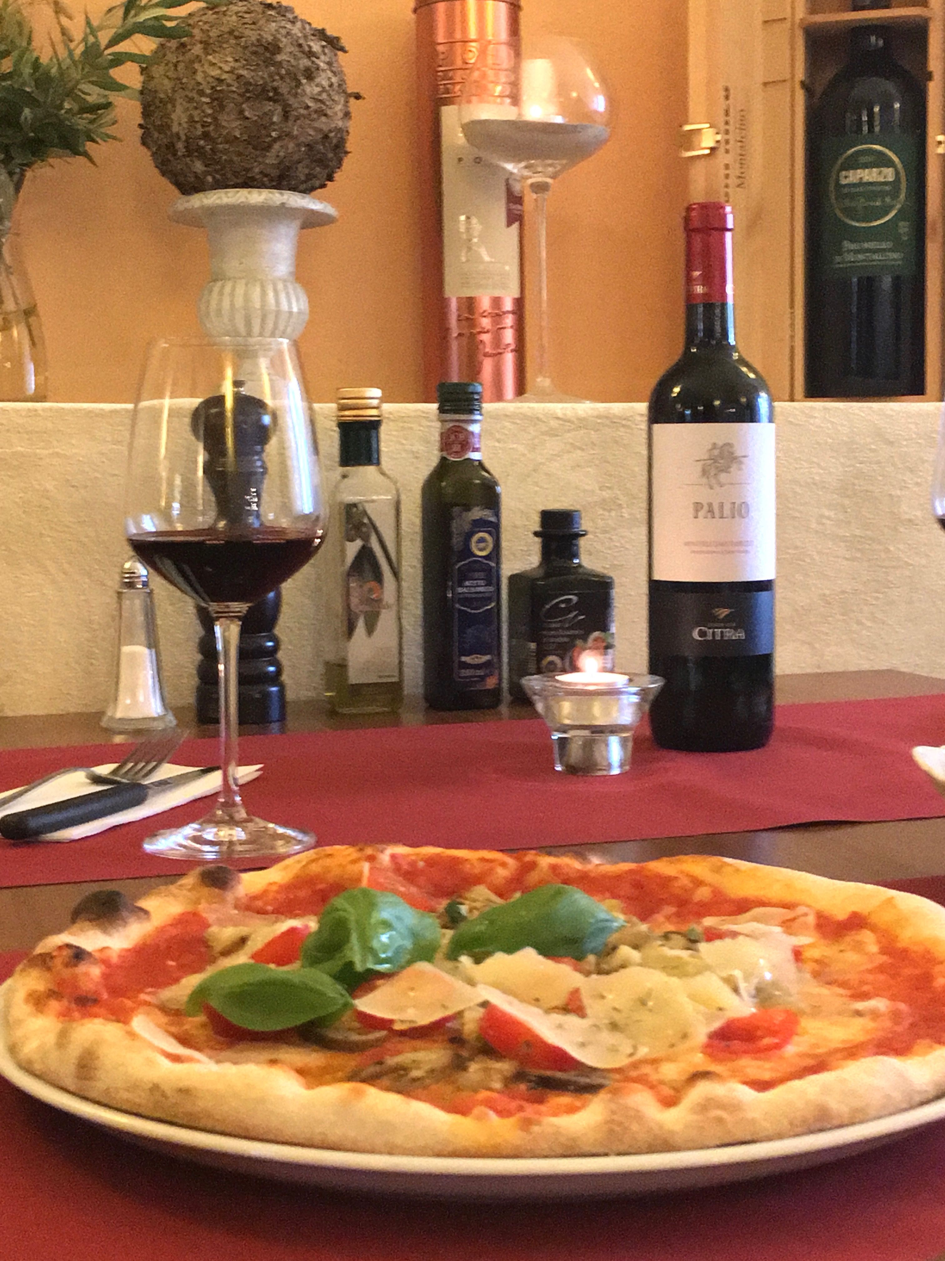 Pizza mit Basilikum und Parmesan auf einem Tisch mit Rotwein und Olivenöl.