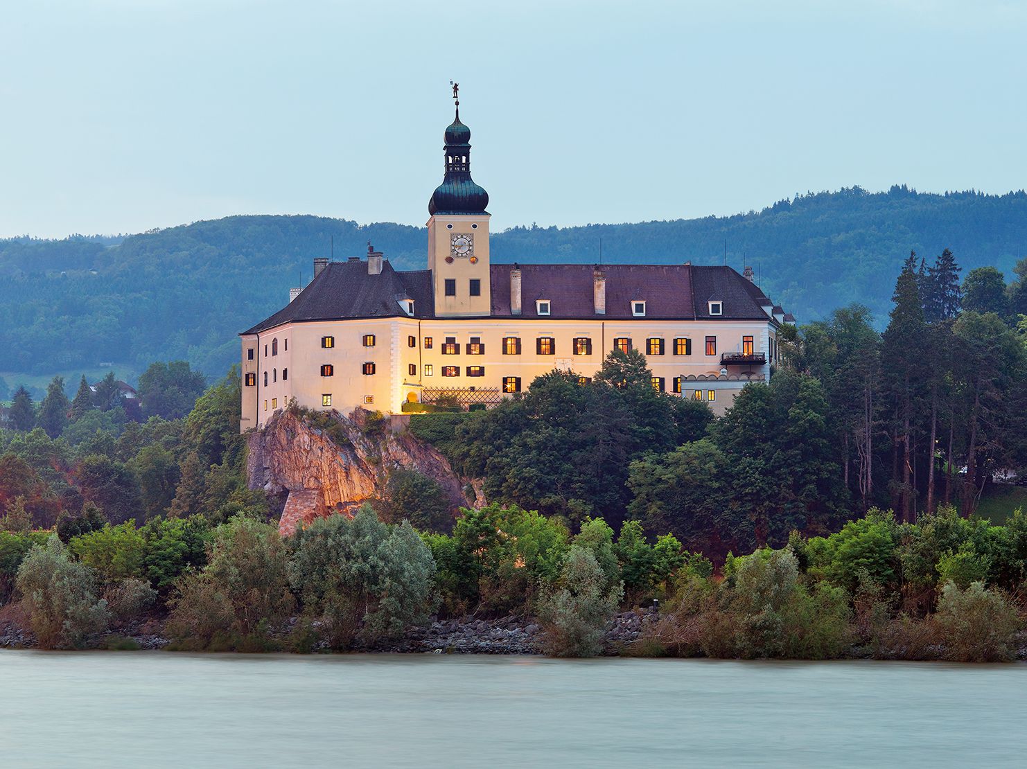 Schloss Persenbeug auf einem Hügel mit Fluss im Vordergrund.