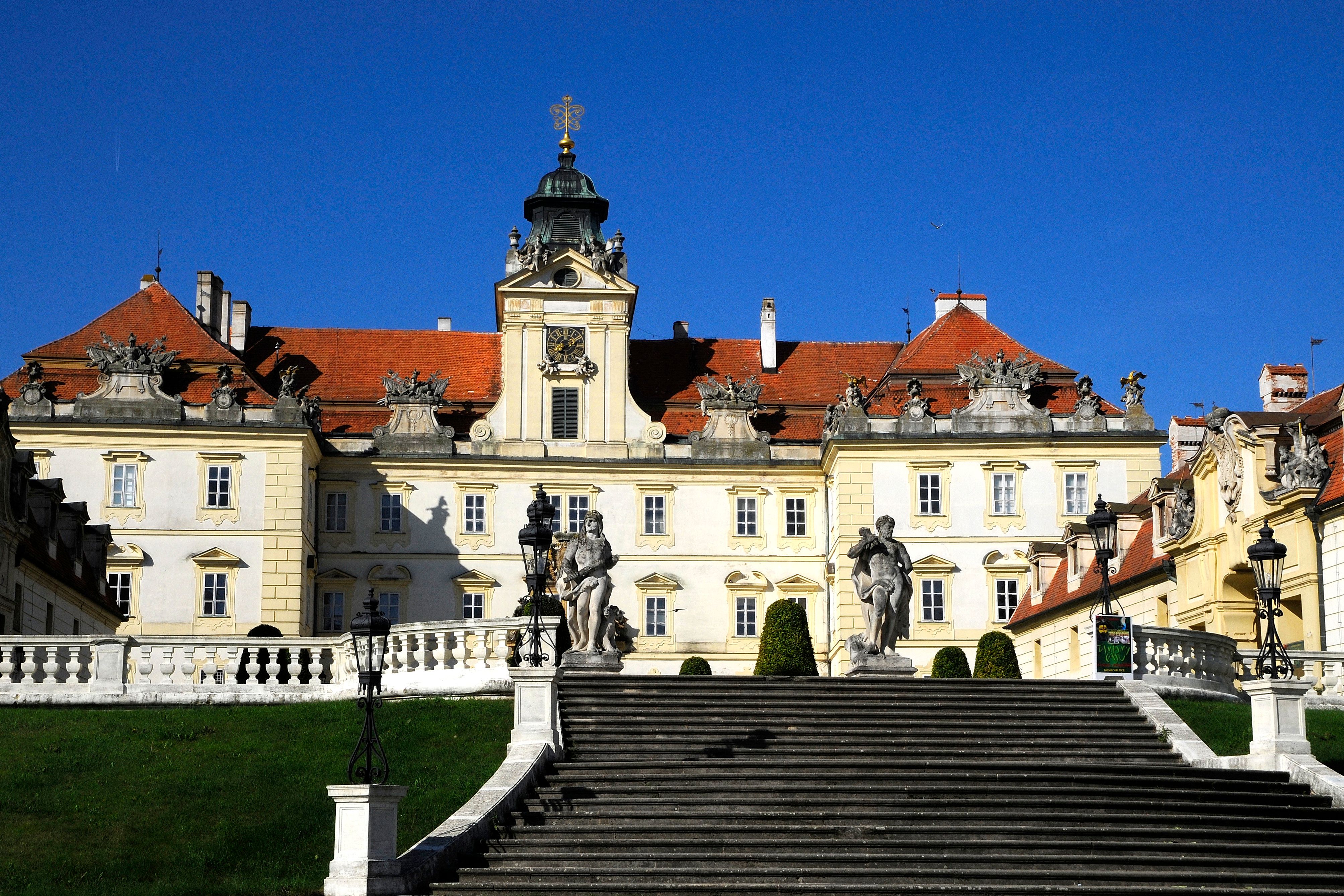 Frontansicht des Schlosses Valtice mit Treppen und Statuen im Vordergrund.