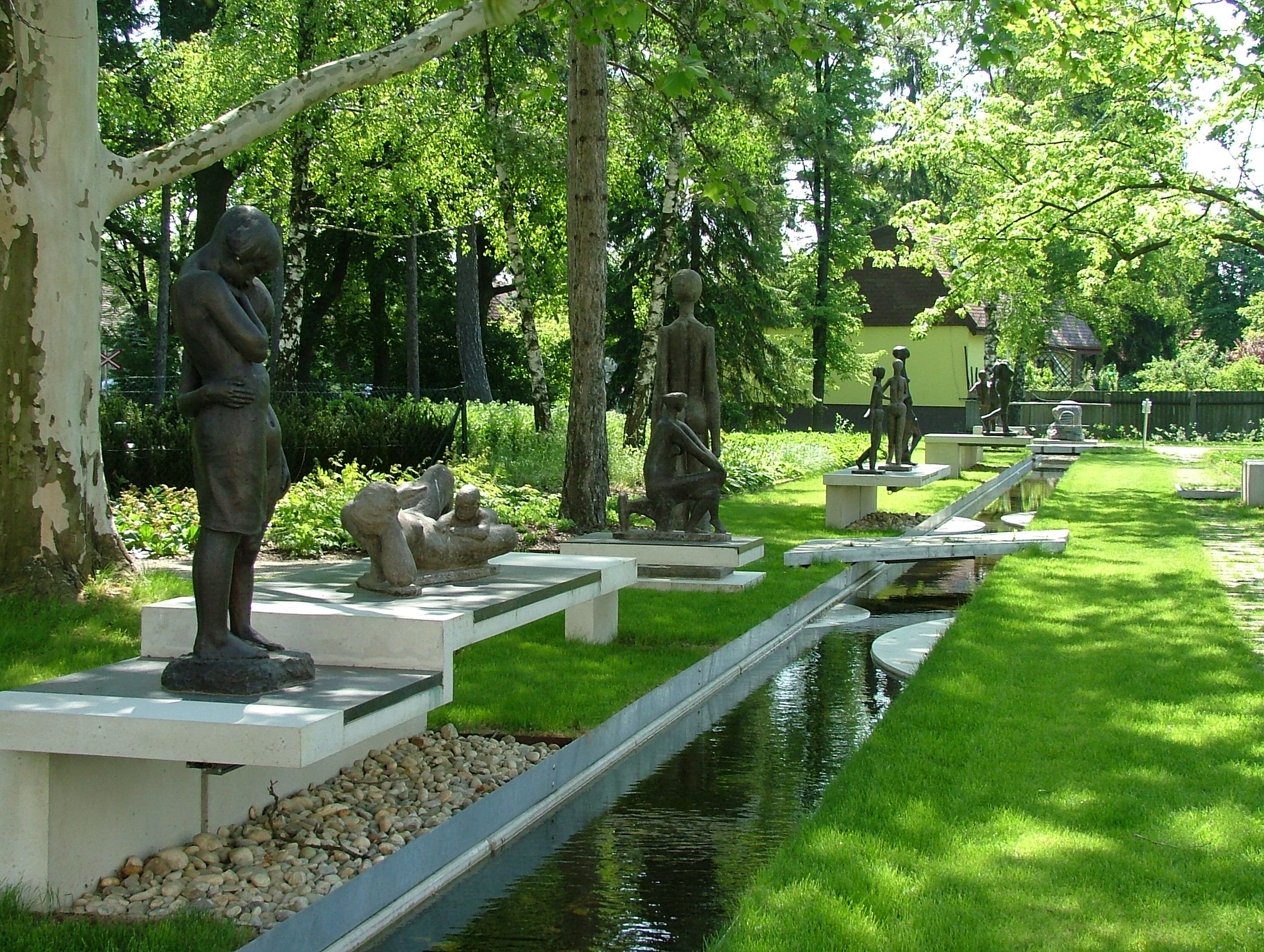 Skulpturen im Park von Bad Pirawarth, umgeben von Bäumen und einem kleinen Wasserlauf.