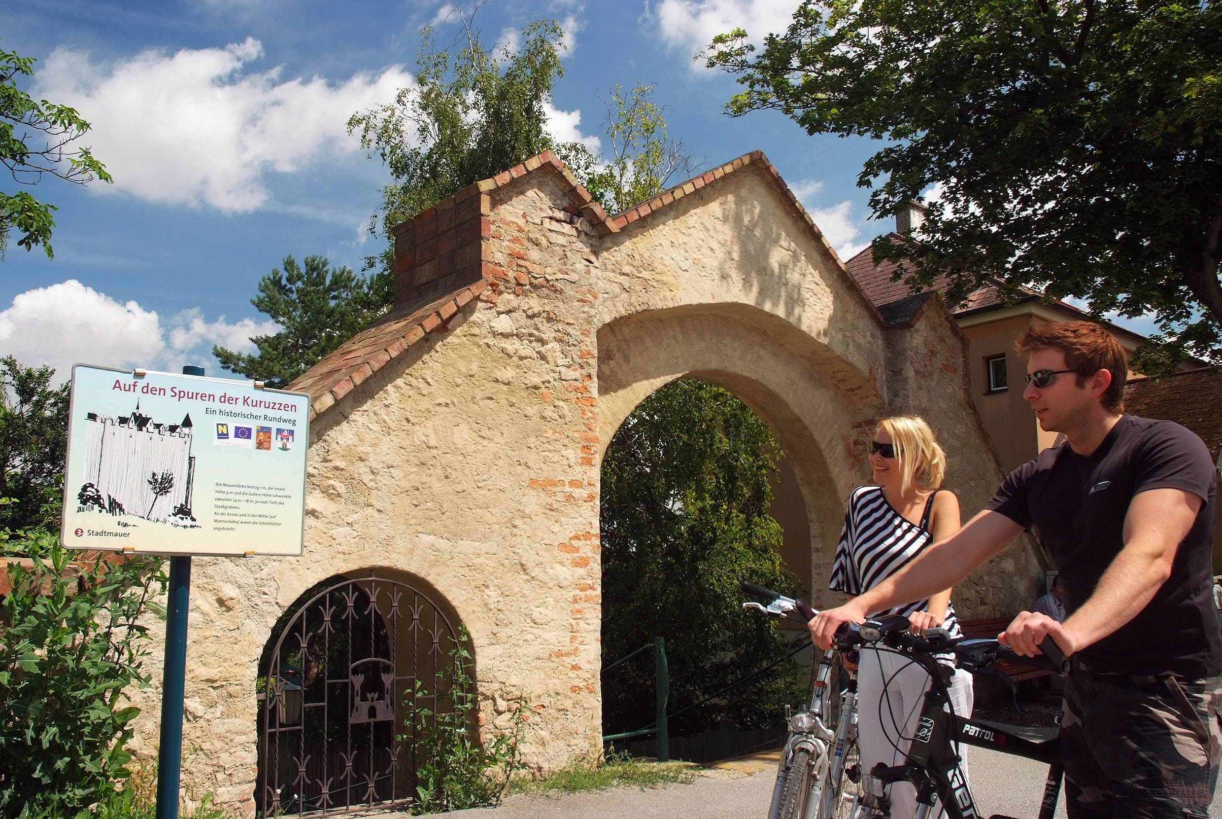 Zwei Personen mit Fahrrädern vor einem historischen Torbogen in Zistersdorf.