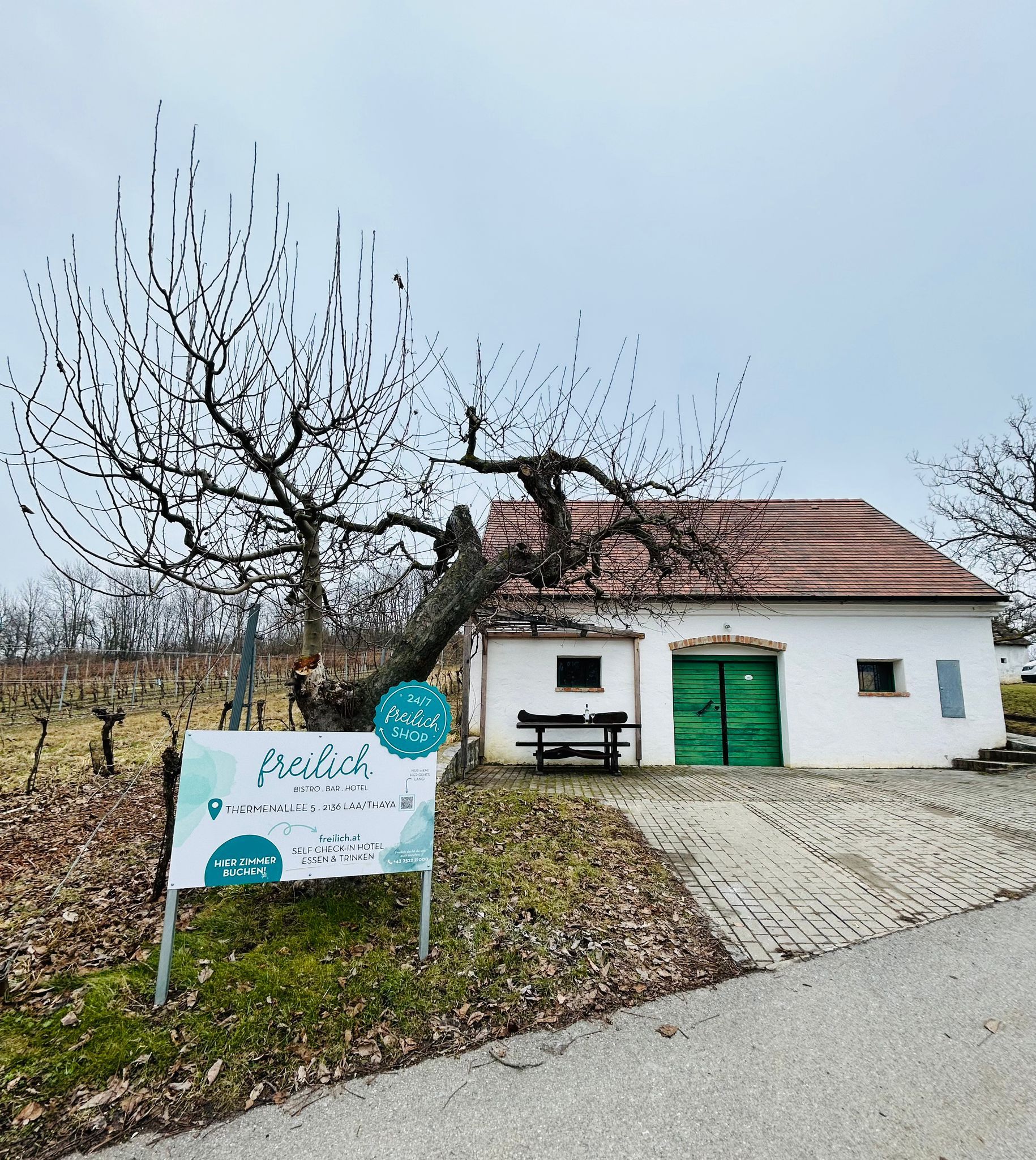 Weißes Gebäude mit grünem Tor und Schild 'freilich' in einer ländlichen Umgebung.