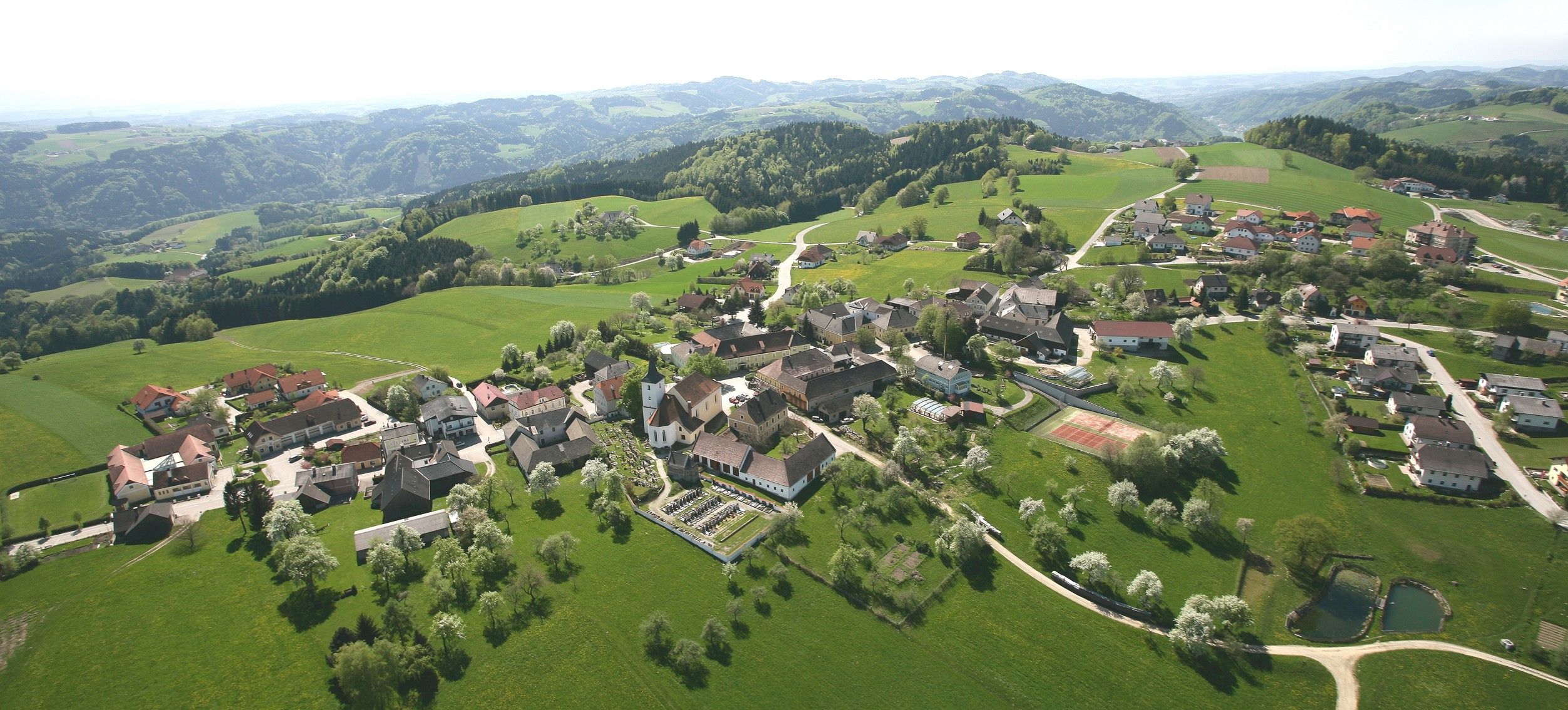 Luftaufnahme der Gemeinde Nöchling mit grünen Feldern und Hügeln.