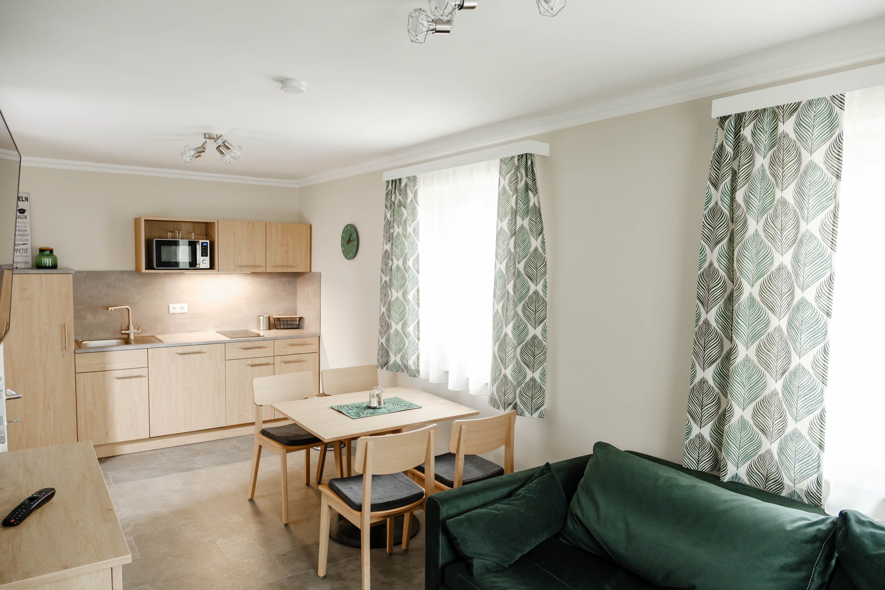 Moderne Küche mit Holzmöbeln, Esstisch, grünen Vorhängen und Sofa.