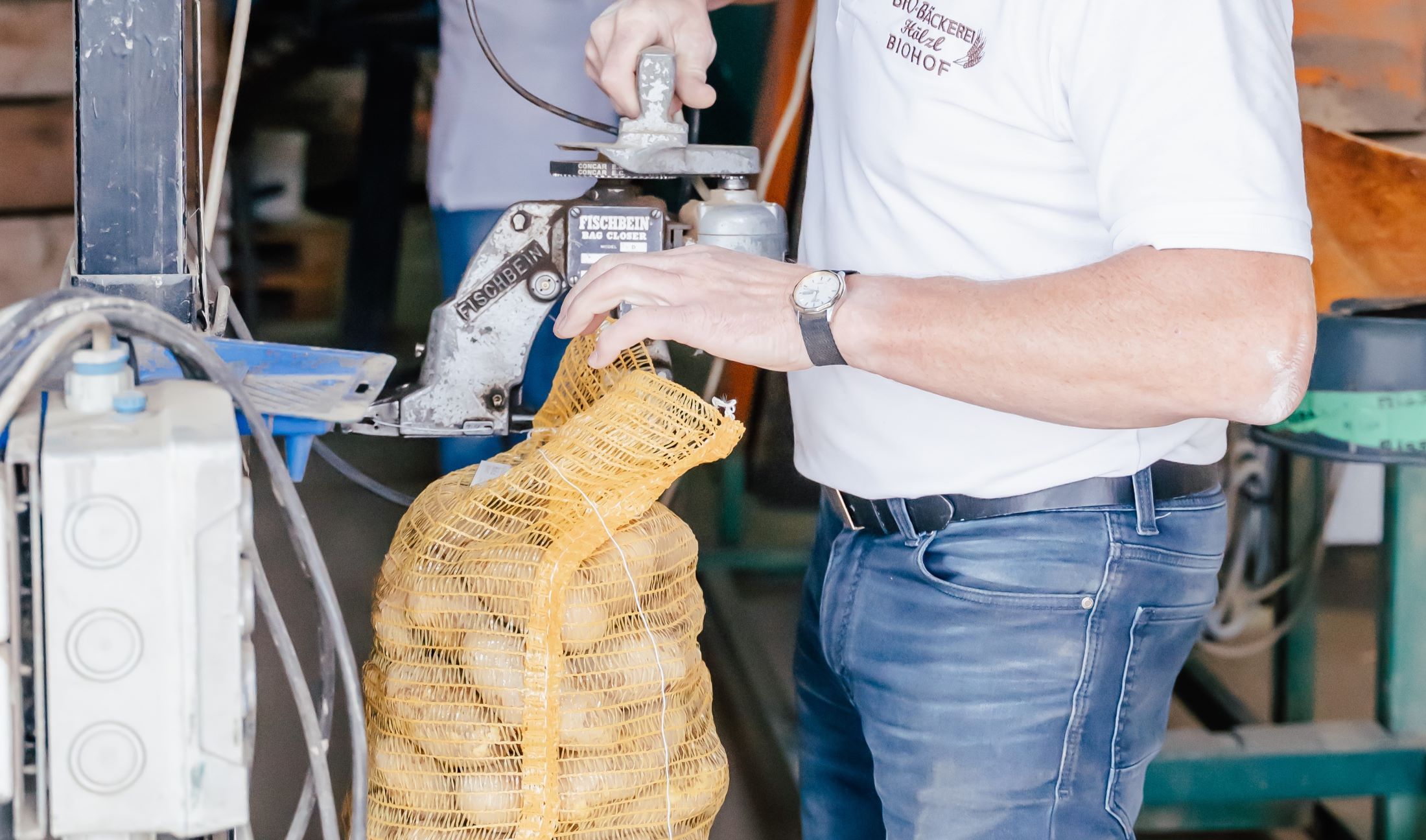 Person verschließt gelben Netzsack mit Maschine.