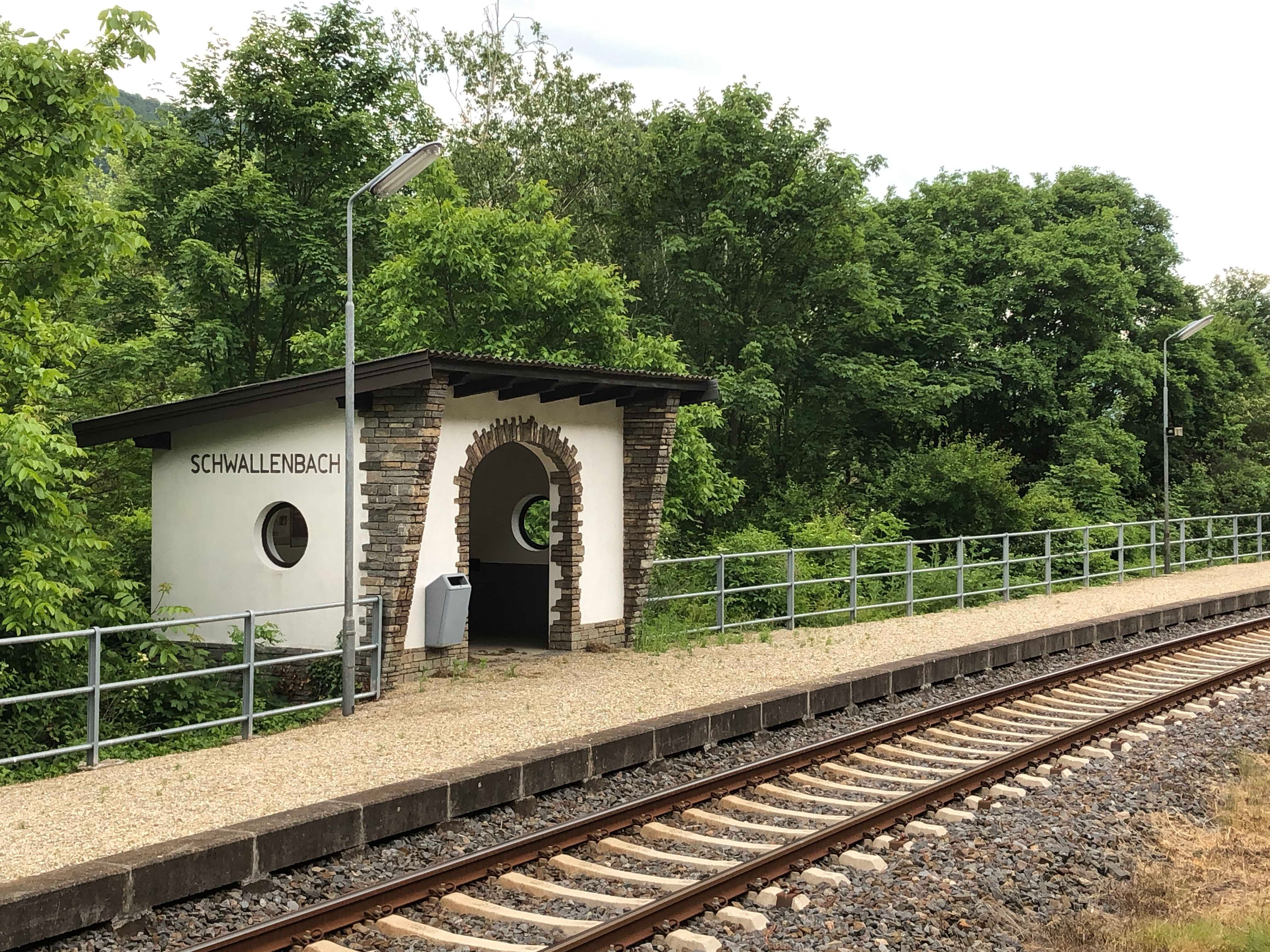 Kleiner Bahnhof Schwallenbach mit Gleisen und umgebender Natur.