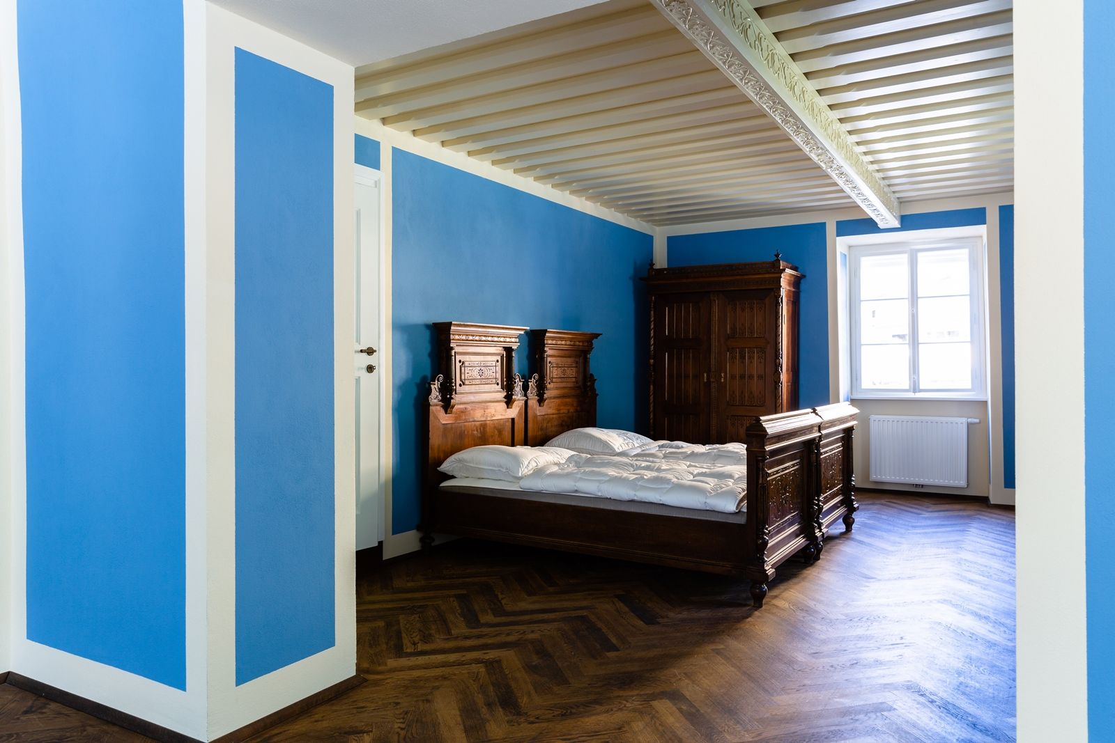 Ein Zimmer mit blauen Wänden, einem Holzbett und einem Schrank.