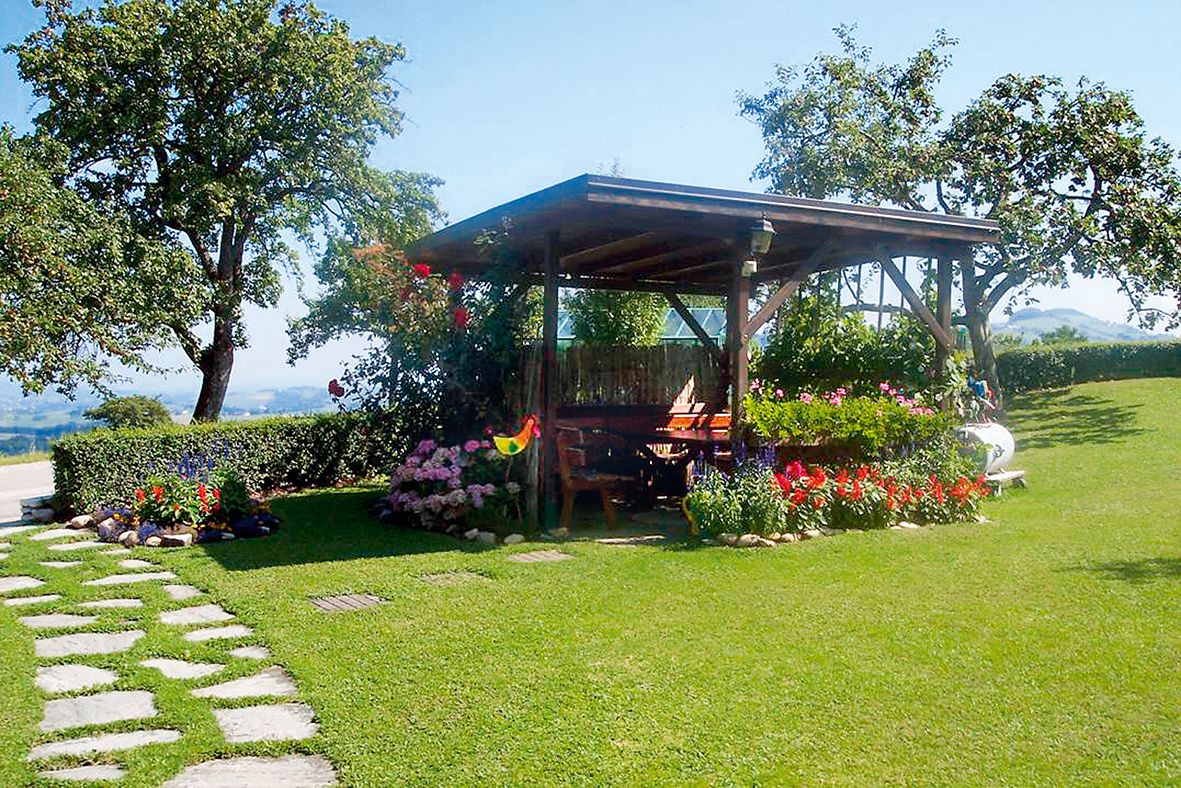 Ein Pavillon auf einem grünen Rasen mit bunten Blumen und Bäumen im Hintergrund.