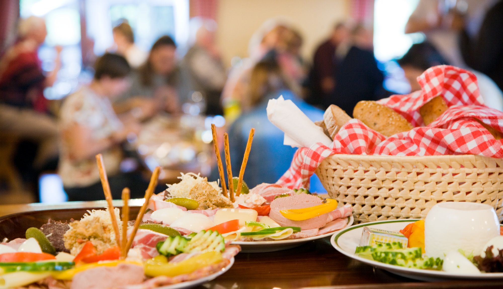 Ein Tisch mit traditionellen österreichischen Speisen, darunter Aufschnitt, Käse und Brot in einem Korb mit rot-weiß kariertem Tuch.