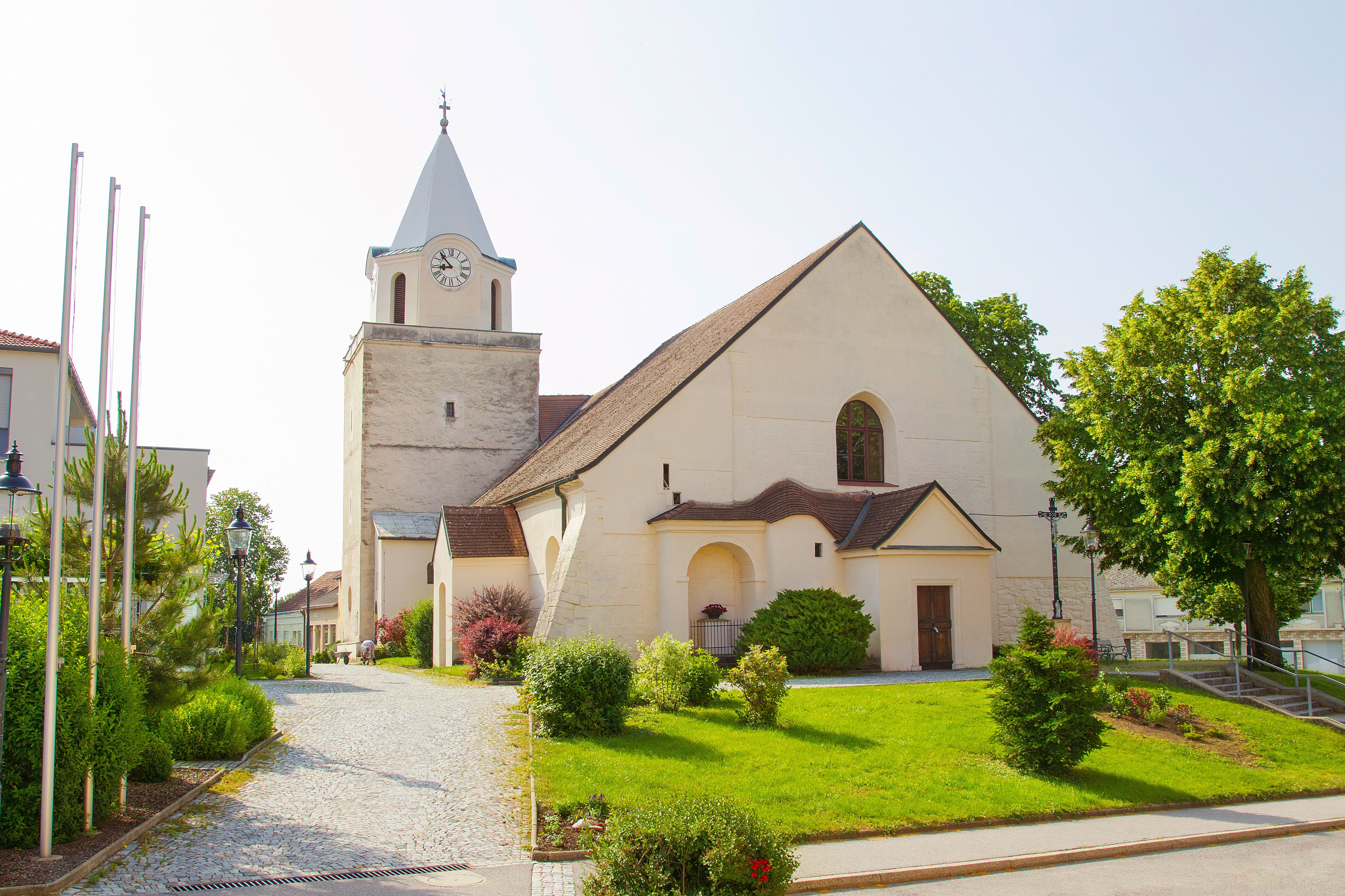 Eine Kirche mit einem Turm und Uhr, umgeben von einem gepflegten Garten und Bäumen.