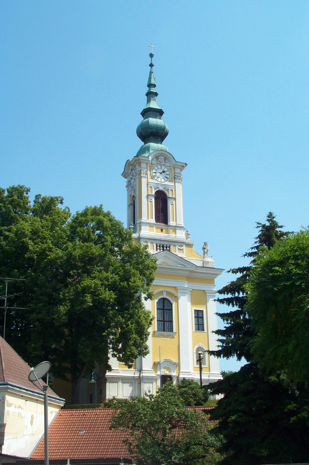 Gelbe Kirche mit Turm und Uhr in Groß-Siegharts, umgeben von Bäumen.