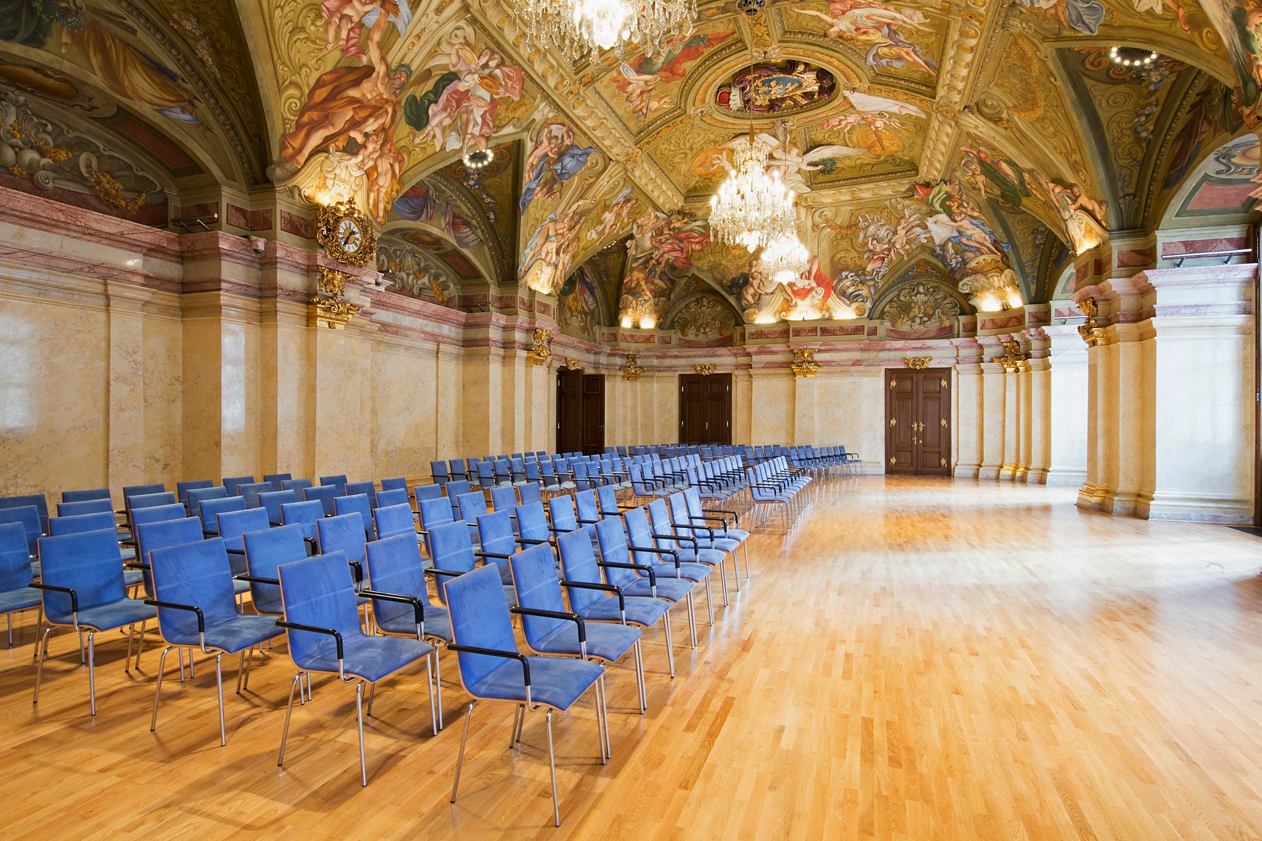 Innenansicht des Landtagssaals im Palais Niederösterreich mit blauen Stühlen und kunstvoll bemalter Decke.
