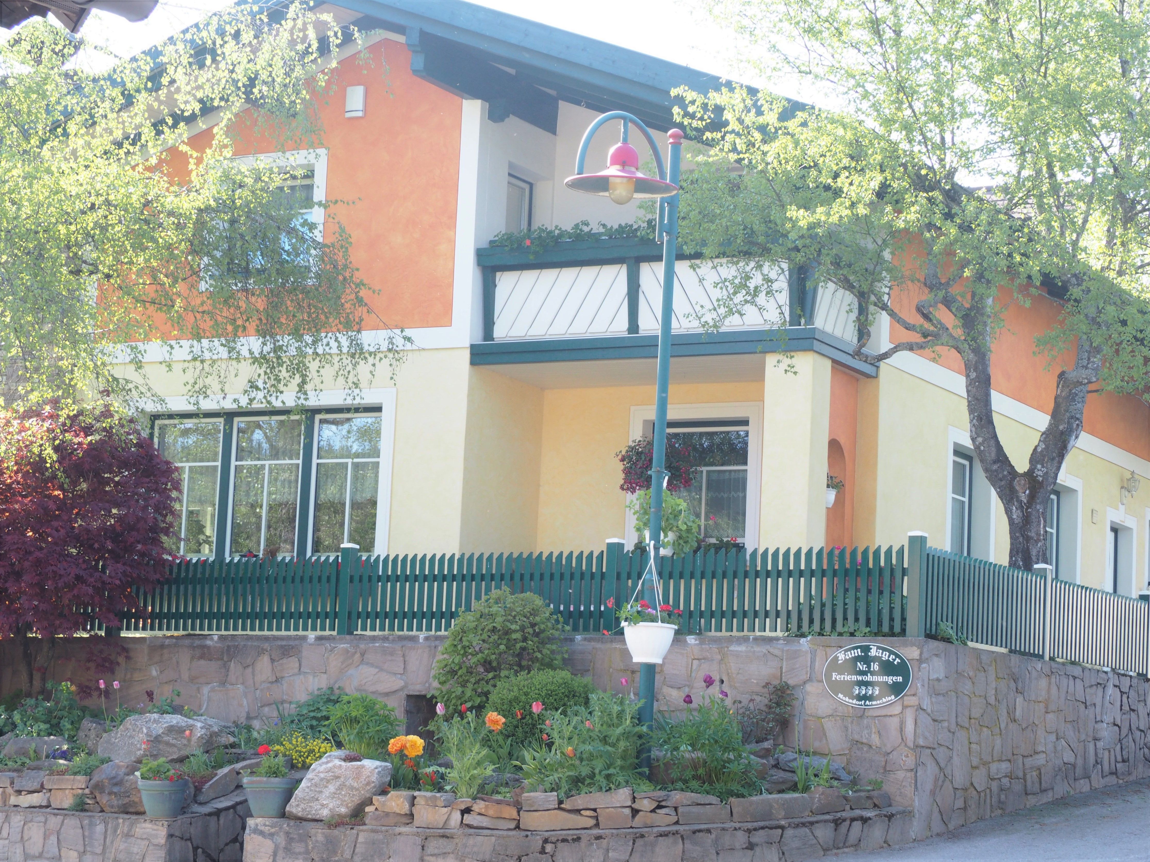 Ein zweistöckiges Haus mit orange-gelber Fassade, grünem Zaun und Garten.