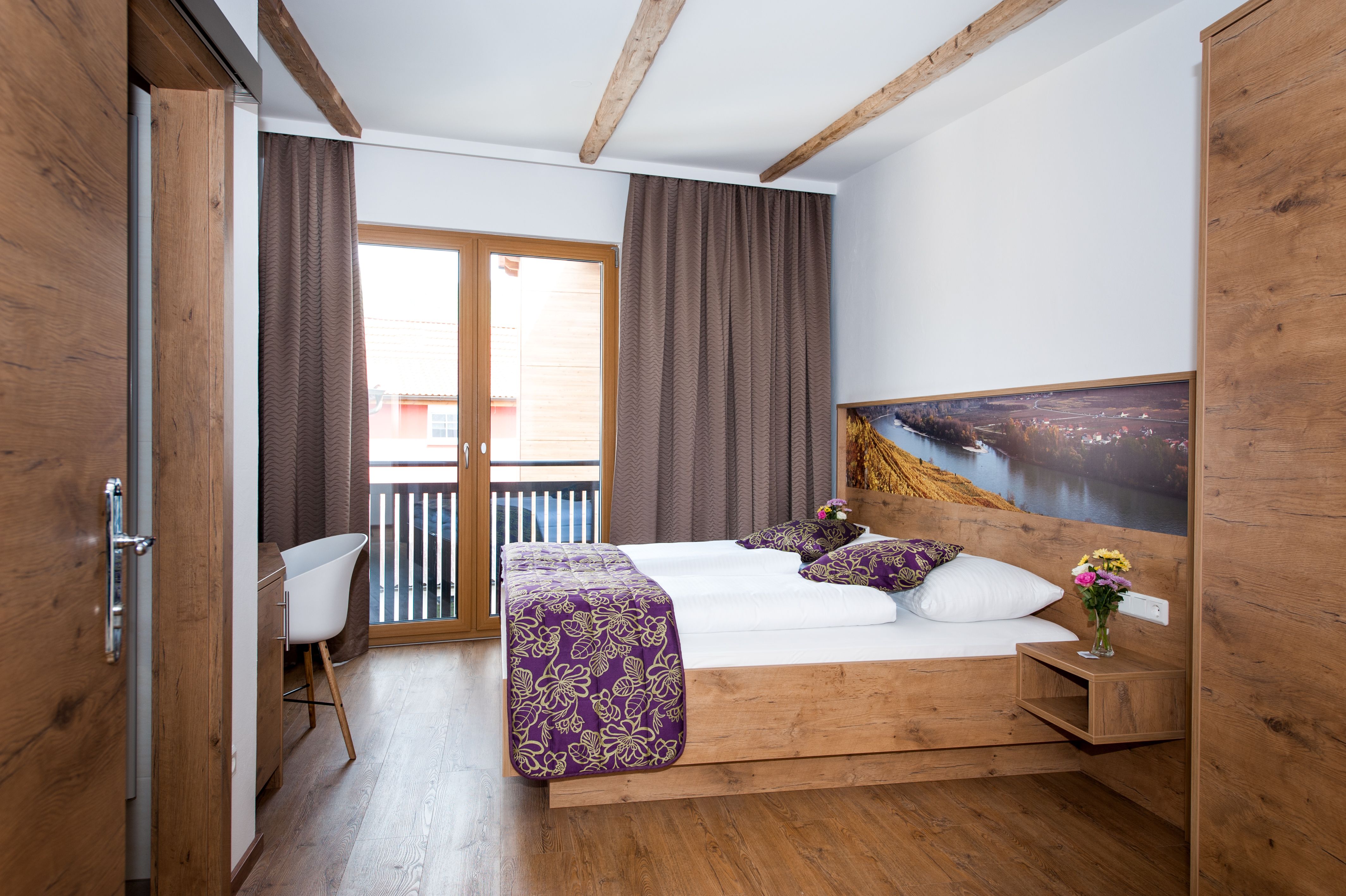 Ein gemütliches Hotelzimmer mit Holzmöbeln, einem Doppelbett, Balkon und dekorativen Kissen.