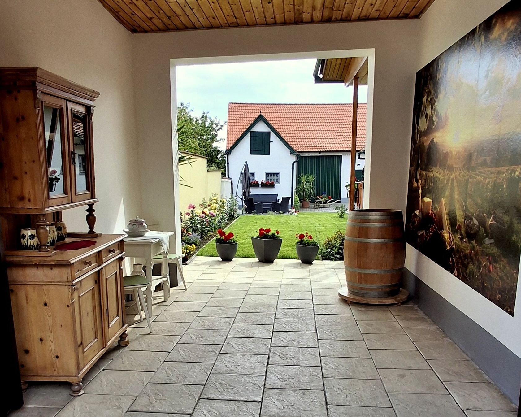 Innenhof mit Holzmöbeln, Pflanzen und Blick auf ein Haus mit rotem Dach.