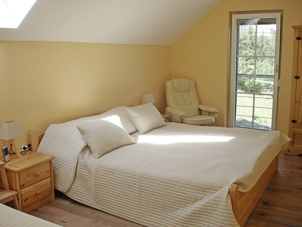 Helles Schlafzimmer mit Doppelbett, Sessel und Fenster mit Blick ins Grüne.
