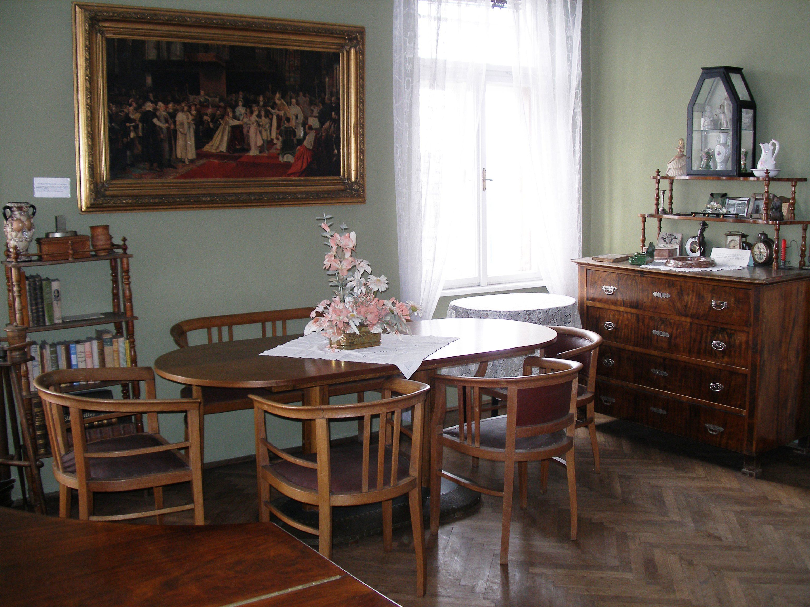 Ein traditionell eingerichtetes Wohnzimmer mit Holzmöbeln, einem runden Tisch, Stühlen, einer Kommode und einem großen Gemälde an der Wand.