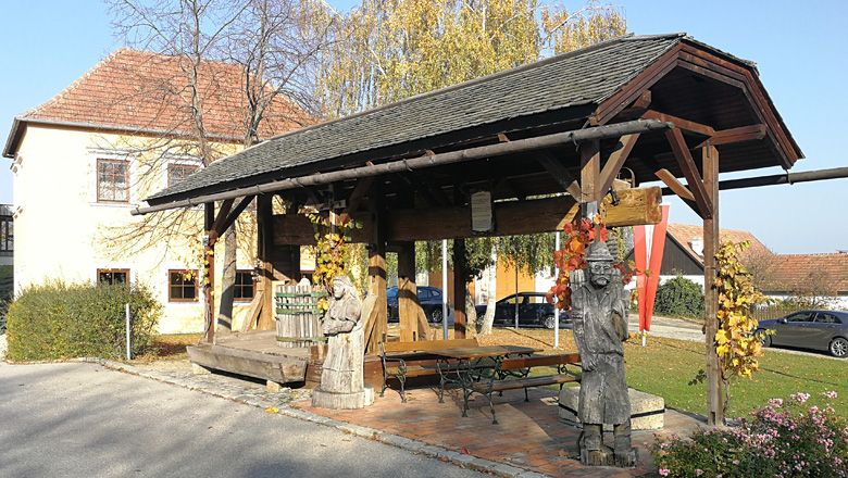 Historische Baumpresse mit Holzfiguren in Droß, umgeben von herbstlicher Vegetation.