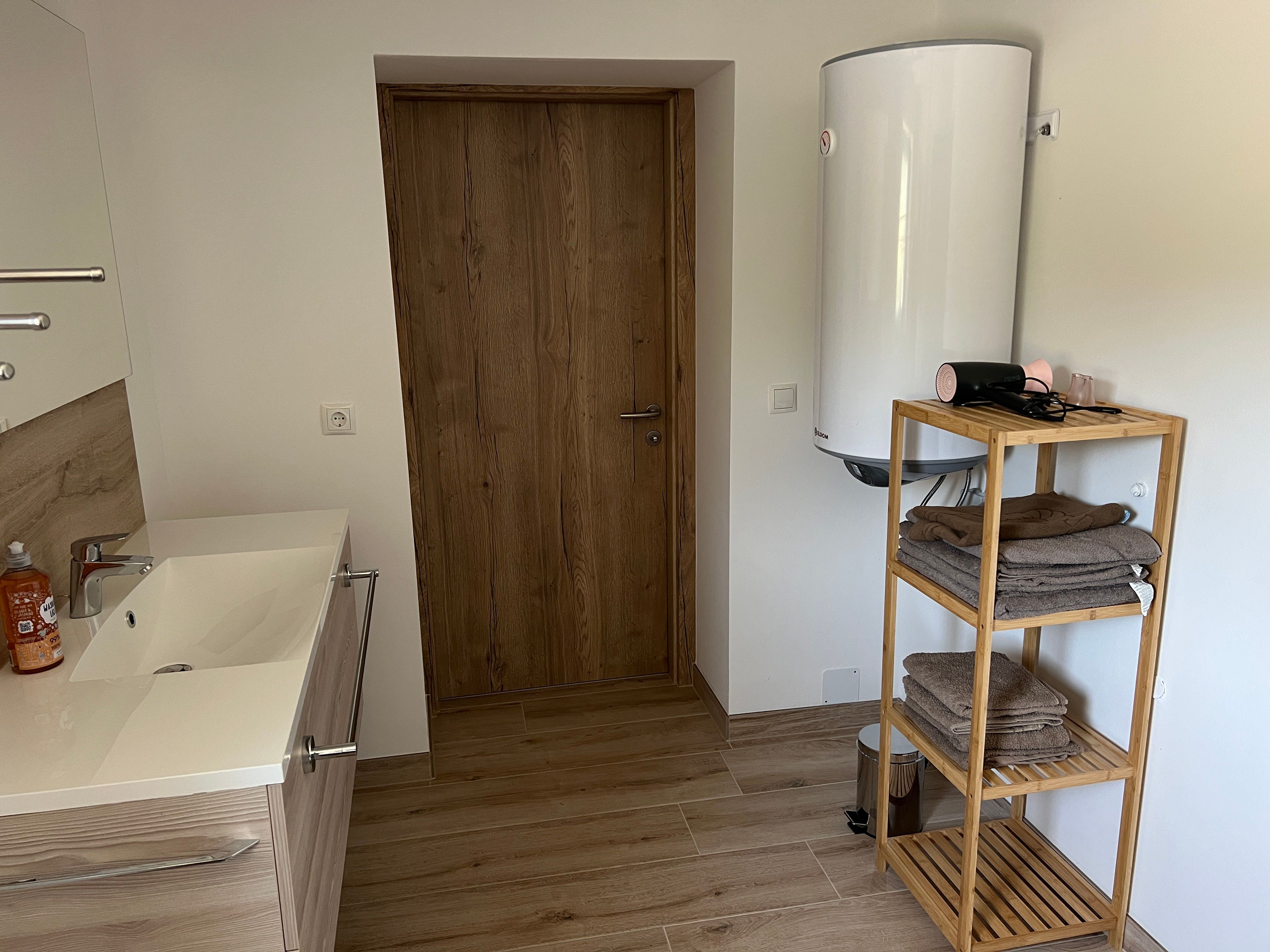 Modernes Badezimmer mit Holzregal, Handtüchern, Waschbecken und Warmwasserboiler.