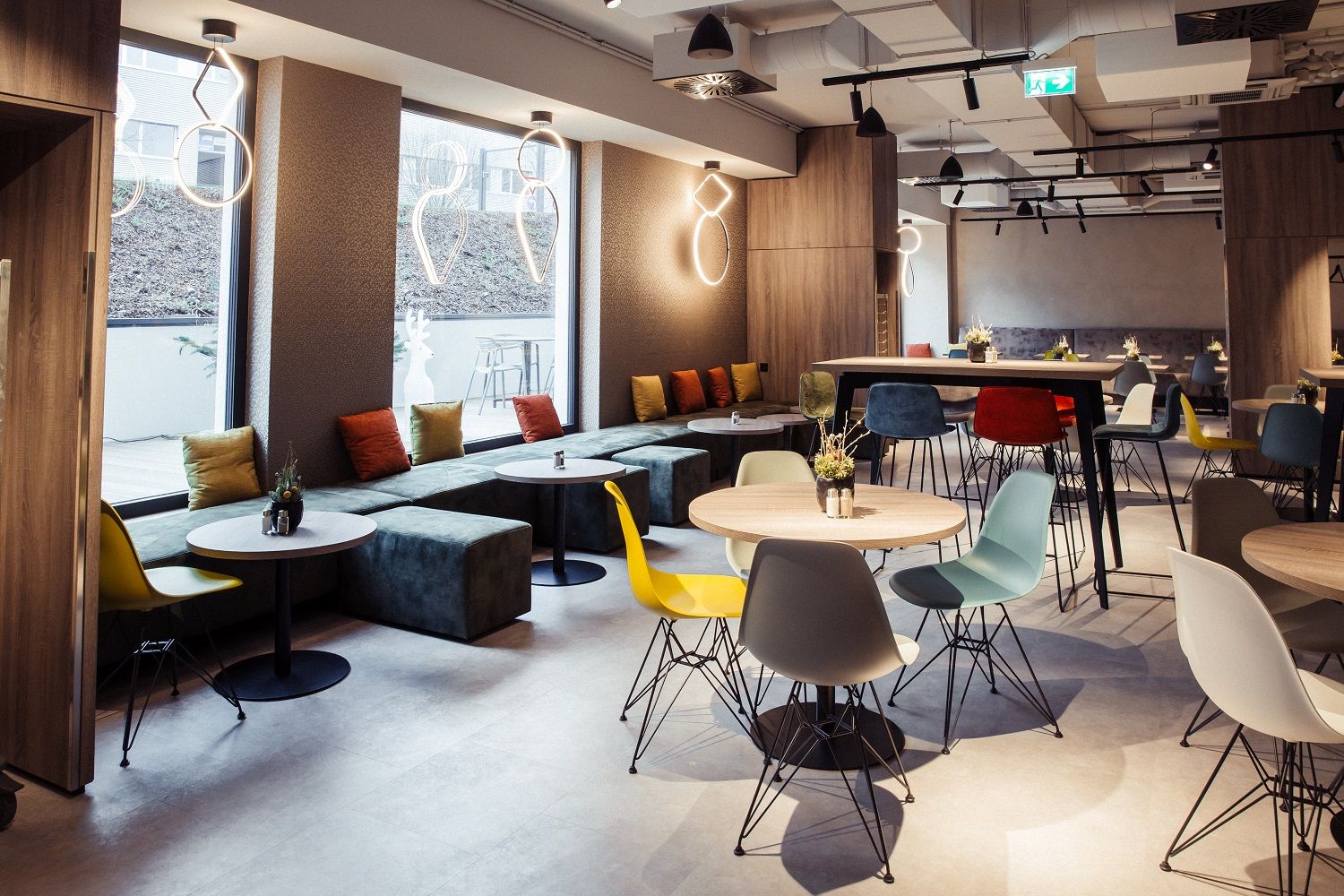 Modernes Hotel-Restaurant mit bunten Stühlen und Tischen, großen Fenstern und stilvollen Leuchten.