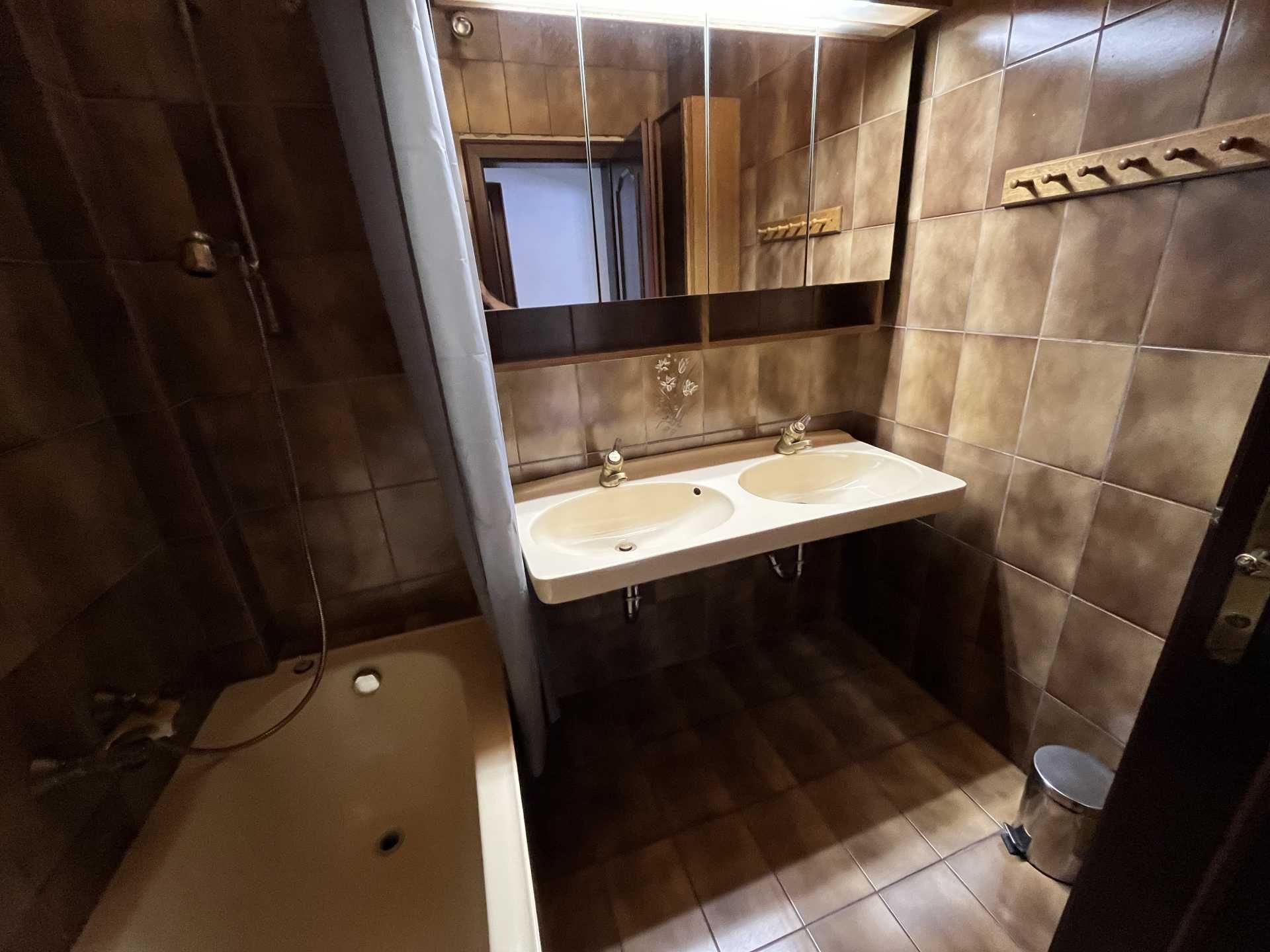 Badezimmer mit braunen Fliesen, Doppelwaschbecken, Badewanne und Spiegel.