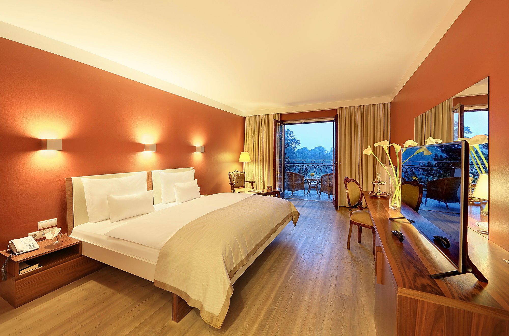 Modernes Hotelzimmer mit Doppelbett, warmen Wandfarben, Balkon und Blick ins Grüne.