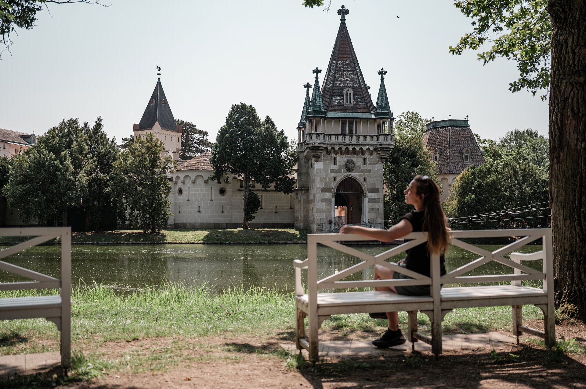 In der warmen Sommerluft sitzt eine junge Frau entspannt auf einer Bank und genießt den Blick auf die majestätischen Gebäude im Hintergrund. Die sanften Wellen des Wassers spiegeln die Schönheit der Natur wider und laden zu einem erholsamen Spaziergang ein. Hier, wo Geschichte und Natur harmonisch verschmelzen, wird jeder Moment zum unvergesslichen Erlebnis.