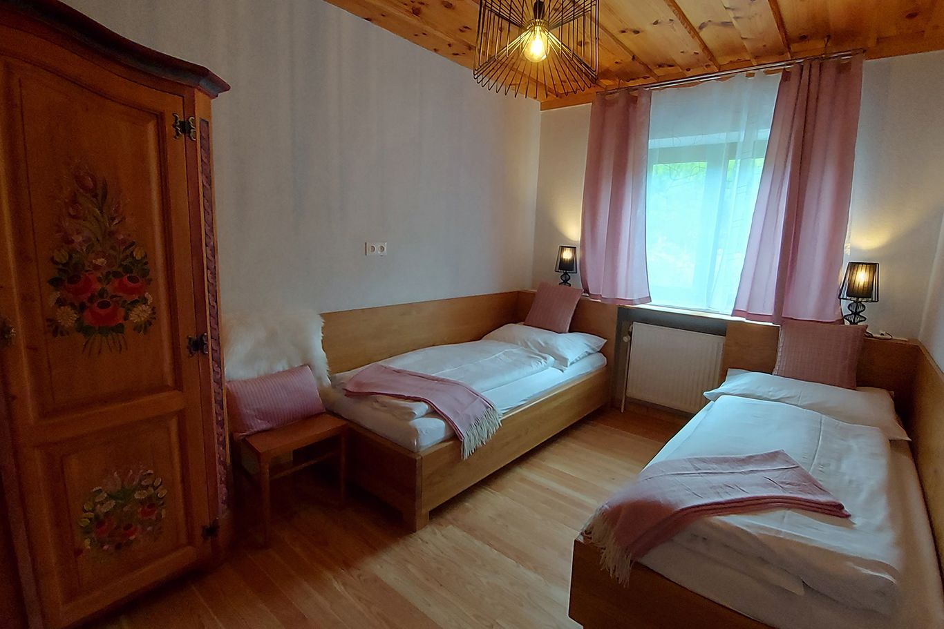 Gemütliches Schlafzimmer mit zwei Einzelbetten, Holzmöbeln und rosa Vorhängen.