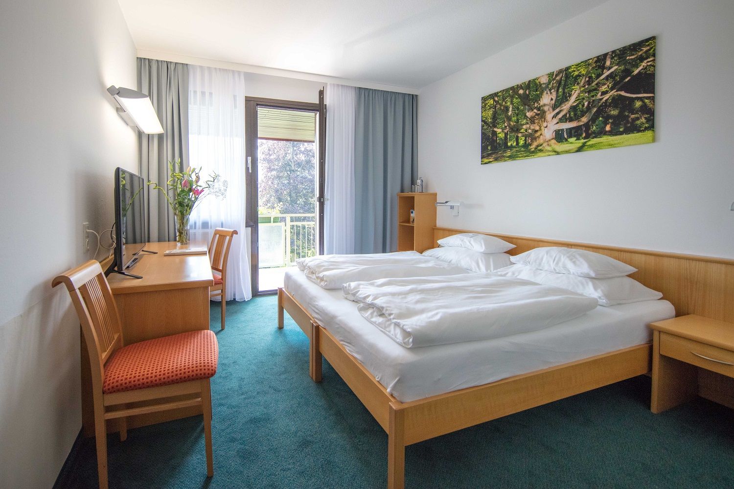 Hotelzimmer mit Doppelbett, Schreibtisch, Stuhl und Balkon.