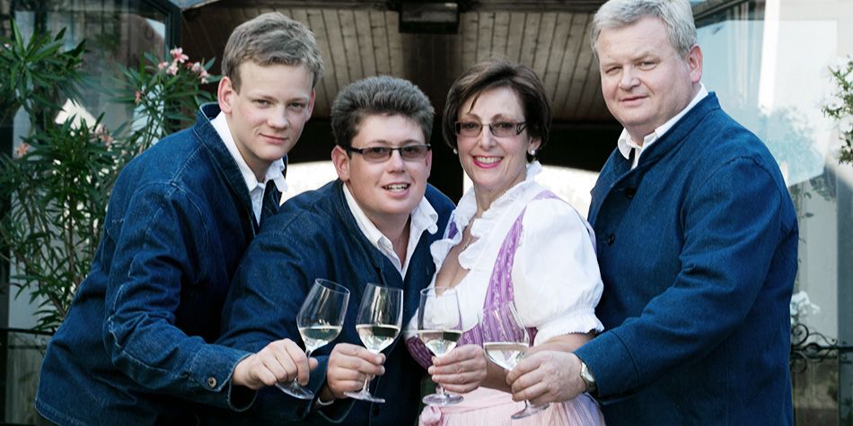 Vier Personen in traditioneller Kleidung stoßen mit Weingläsern an.