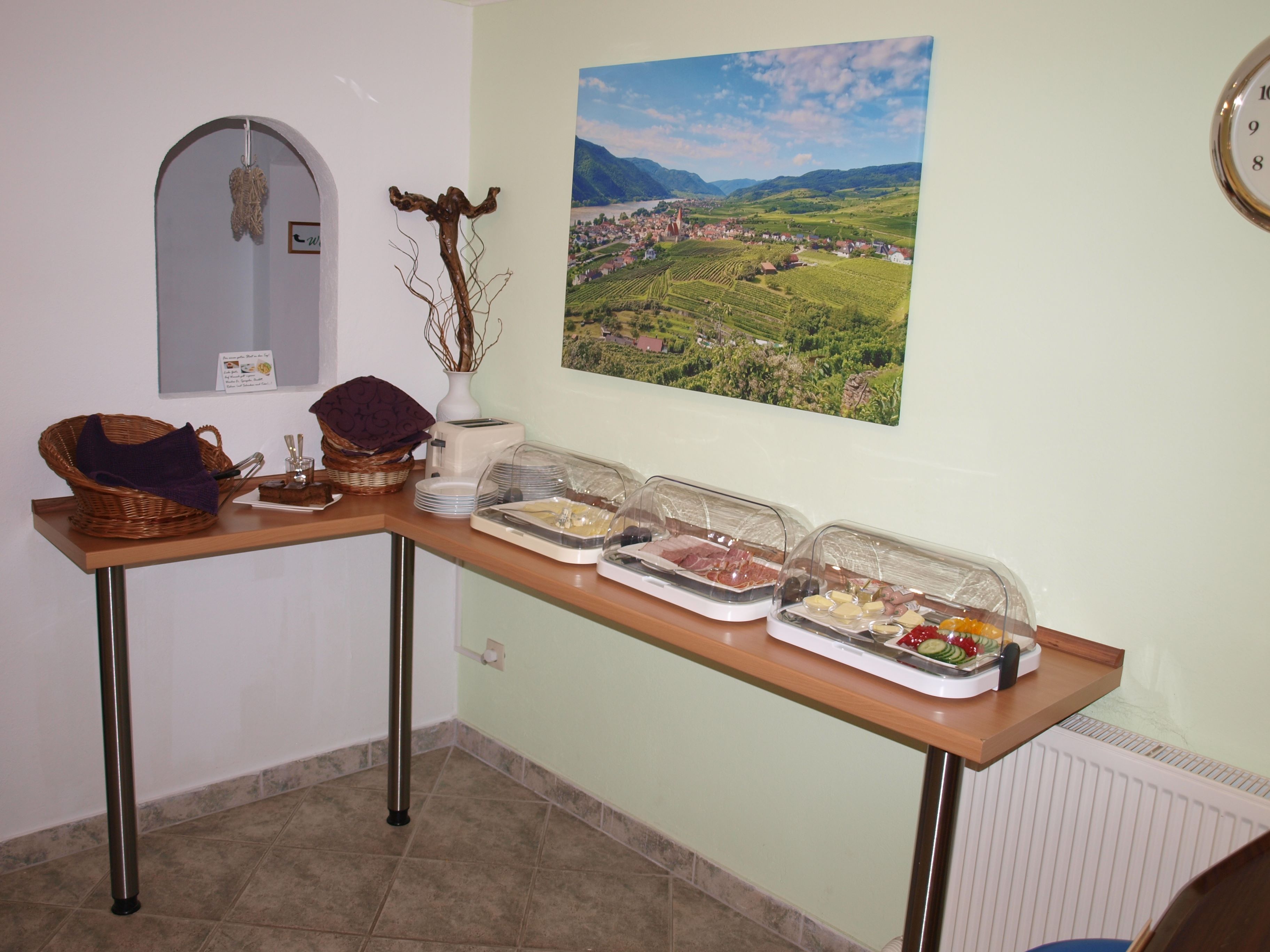 Frühstücksbuffet mit Aufschnitt und Gemüse in einem Raum mit Landschaftsbild an der Wand.