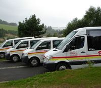 Vier weiße Transporter mit gelben und roten Streifen parken nebeneinander auf einem Parkplatz.