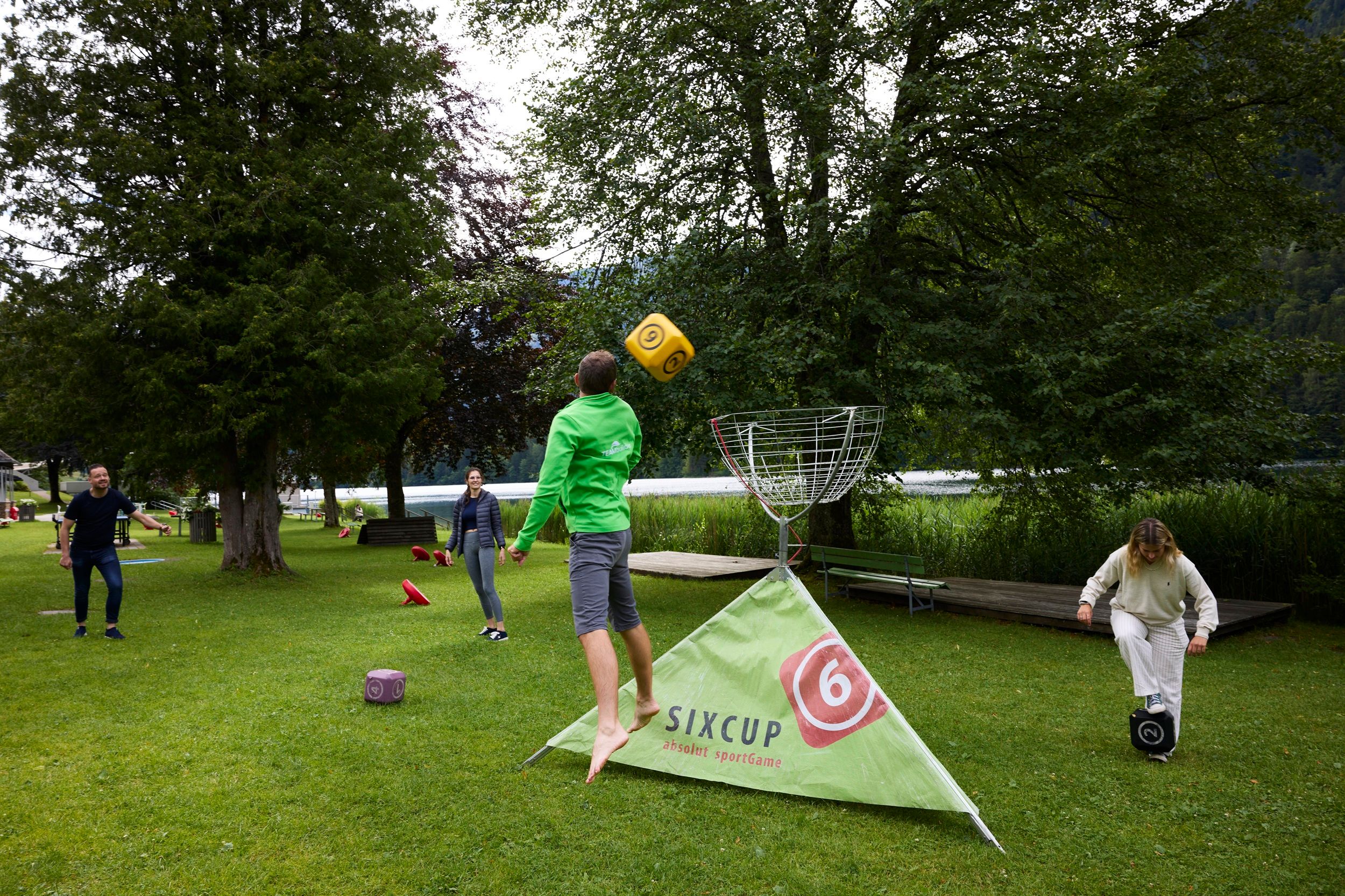 Menschen spielen ein Outdoor-Wurfspiel mit großen Würfeln auf einer Wiese.