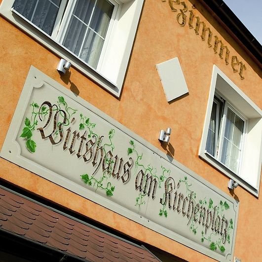 Fassade eines Gebäudes mit dem Schild 'Wirtshaus am Kirchenplatz'.